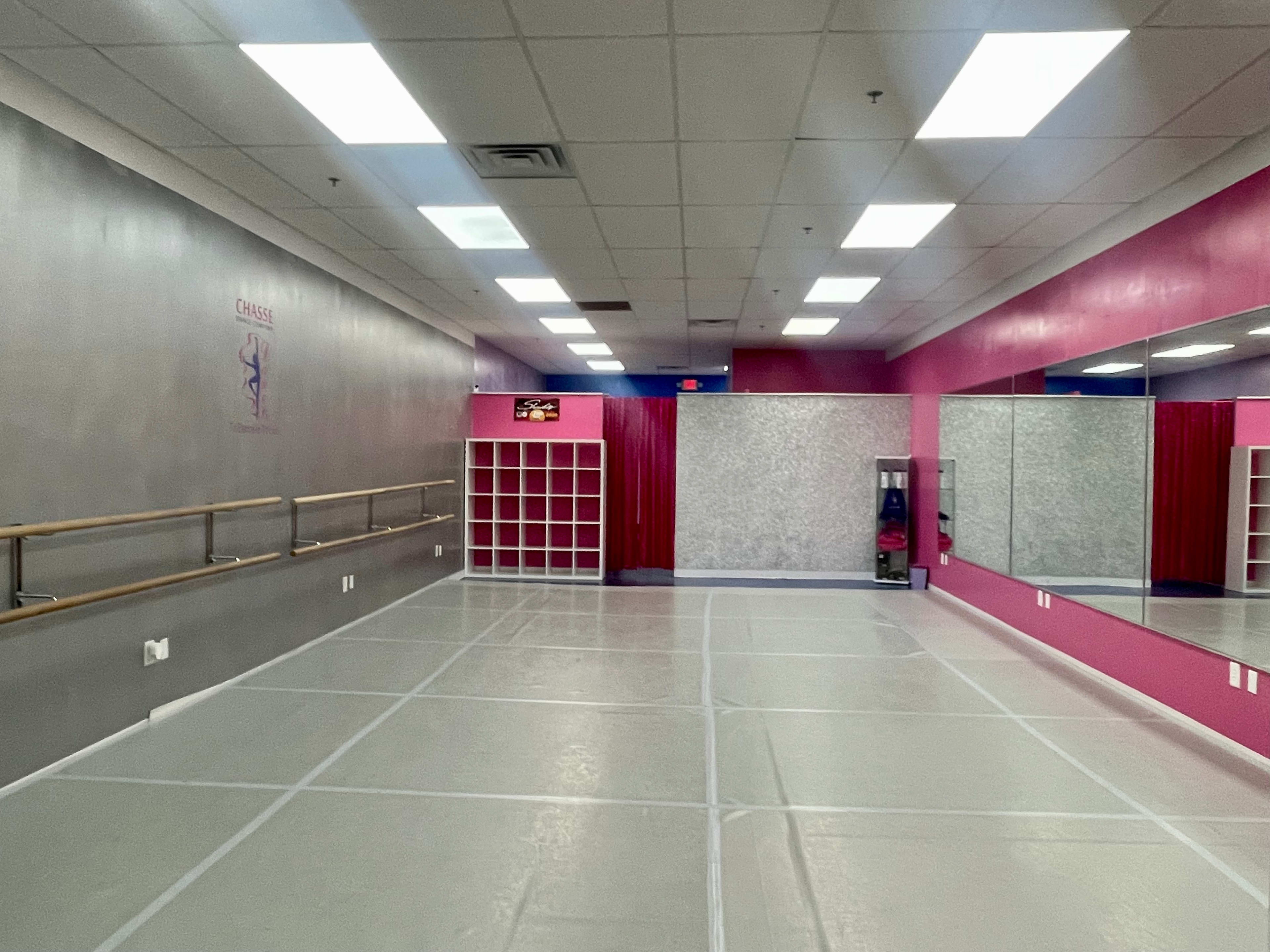 The image displays a dance studio with mirrored walls, a ballet barre, and a section for storage cubbies.