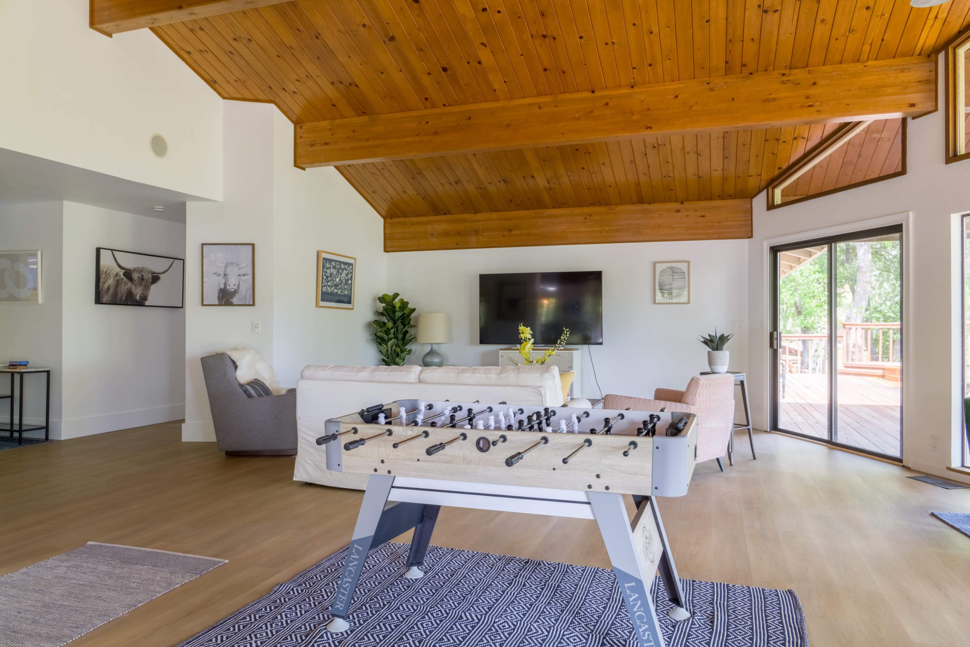 A spacious living area featuring a foosball table, a sectional sofa, and large windows that open to a deck.