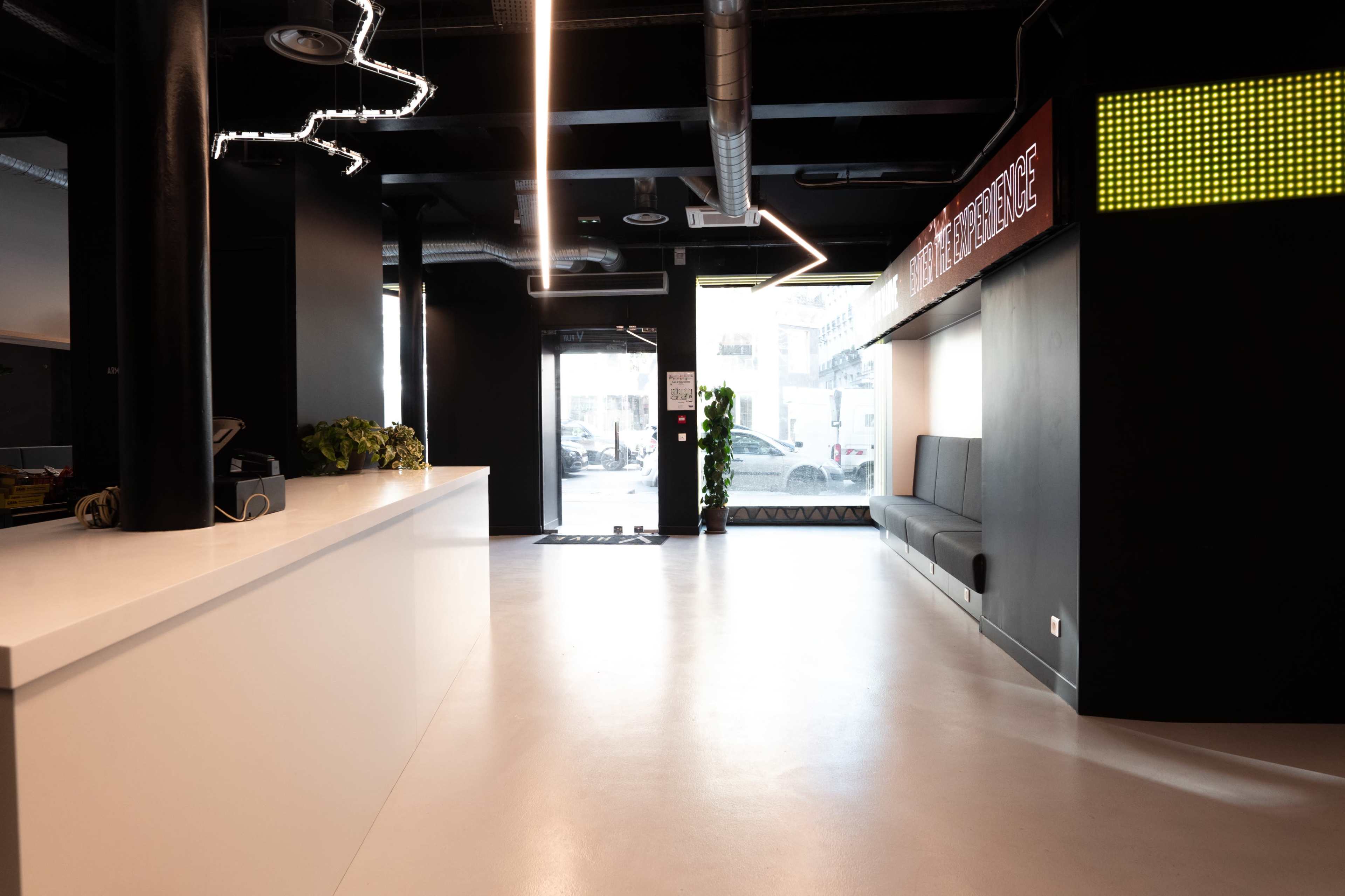 The image shows a modern reception area featuring a sleek white counter, black seating along the wall, and bright signage overhead.