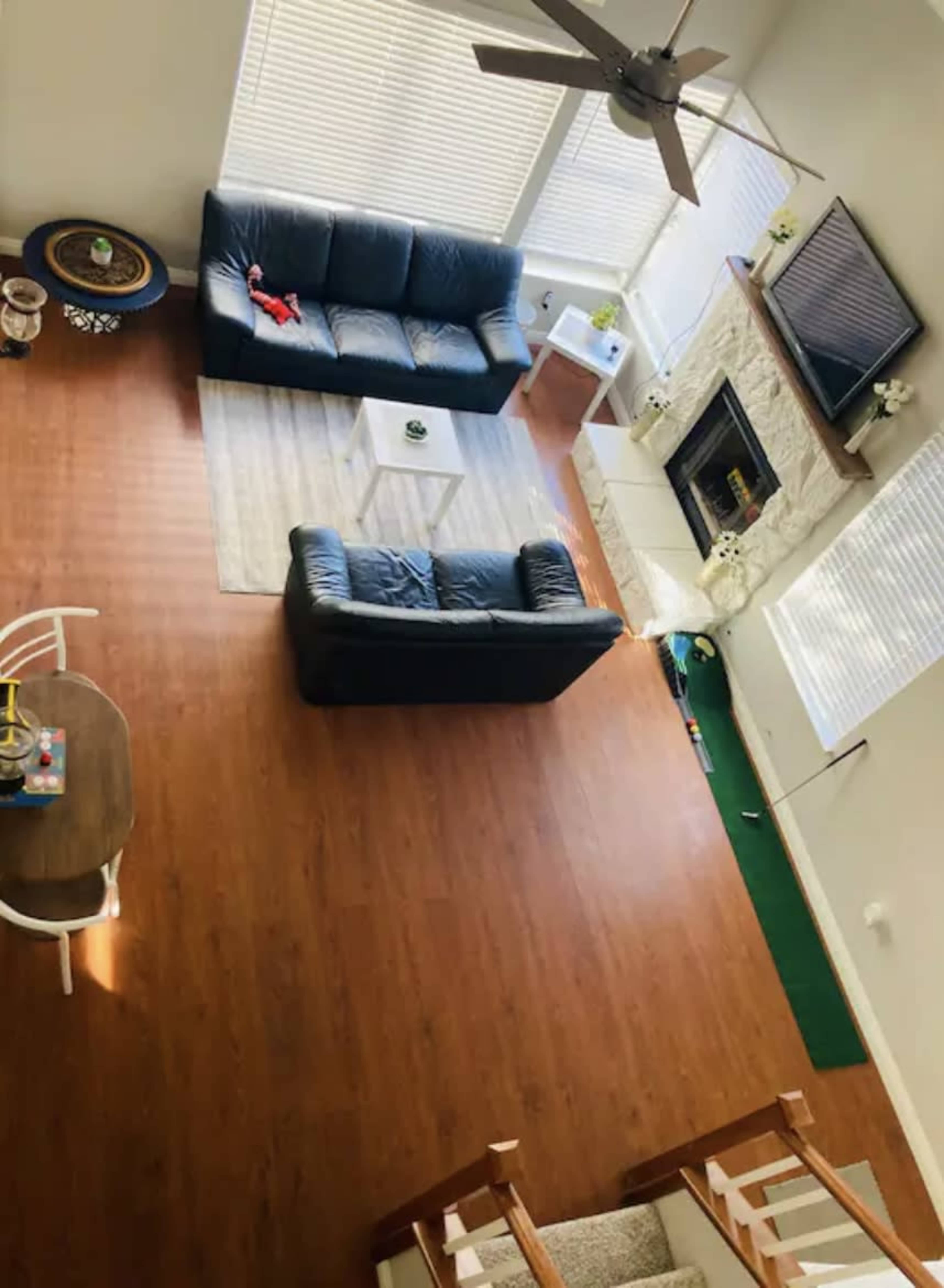 A living room with two black sofas facing a white coffee table and a fireplace, surrounded by wooden flooring and large windows.