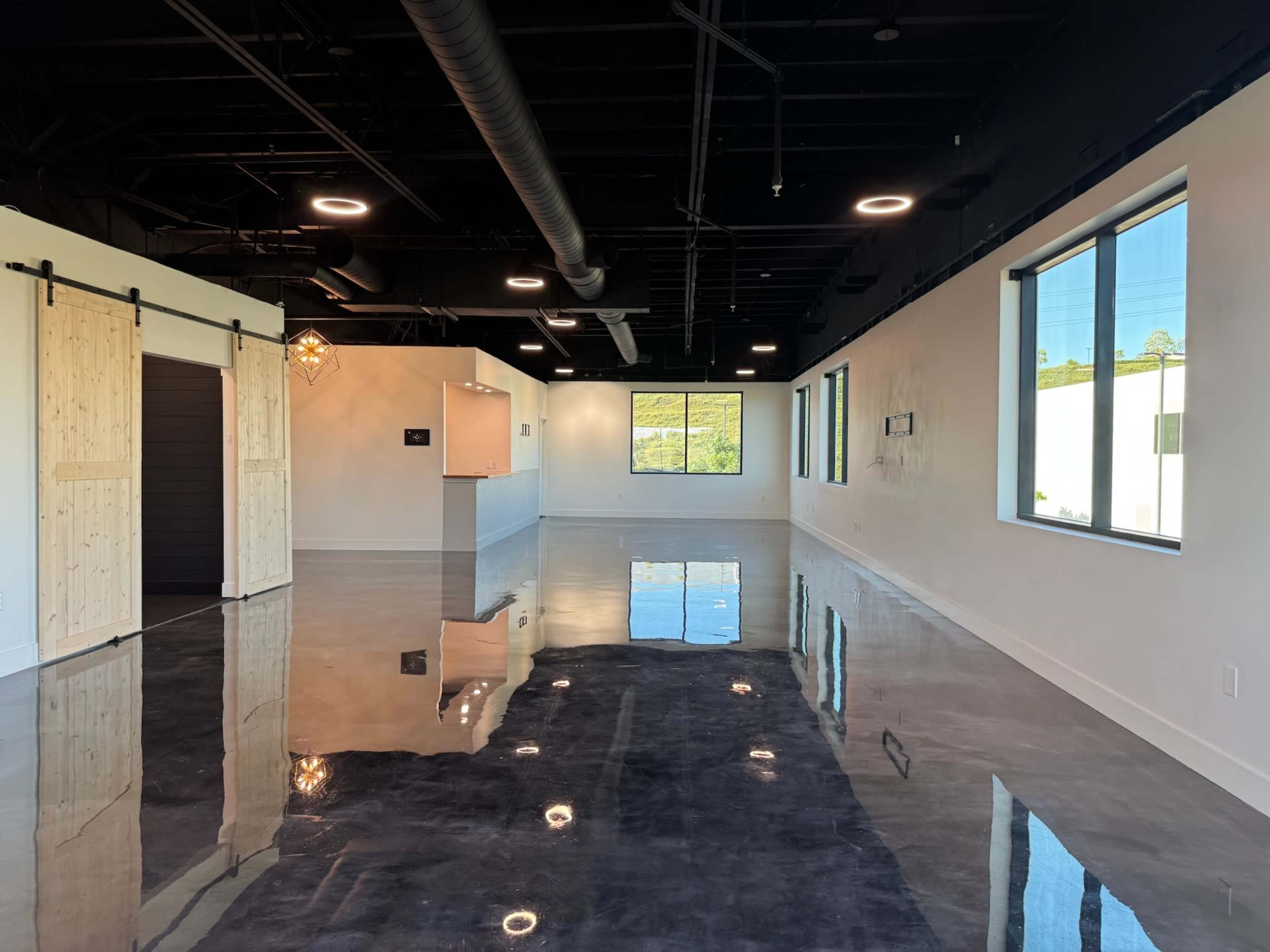 The image depicts a spacious interior with polished concrete floors, large windows, and sliding barn doors along one wall.