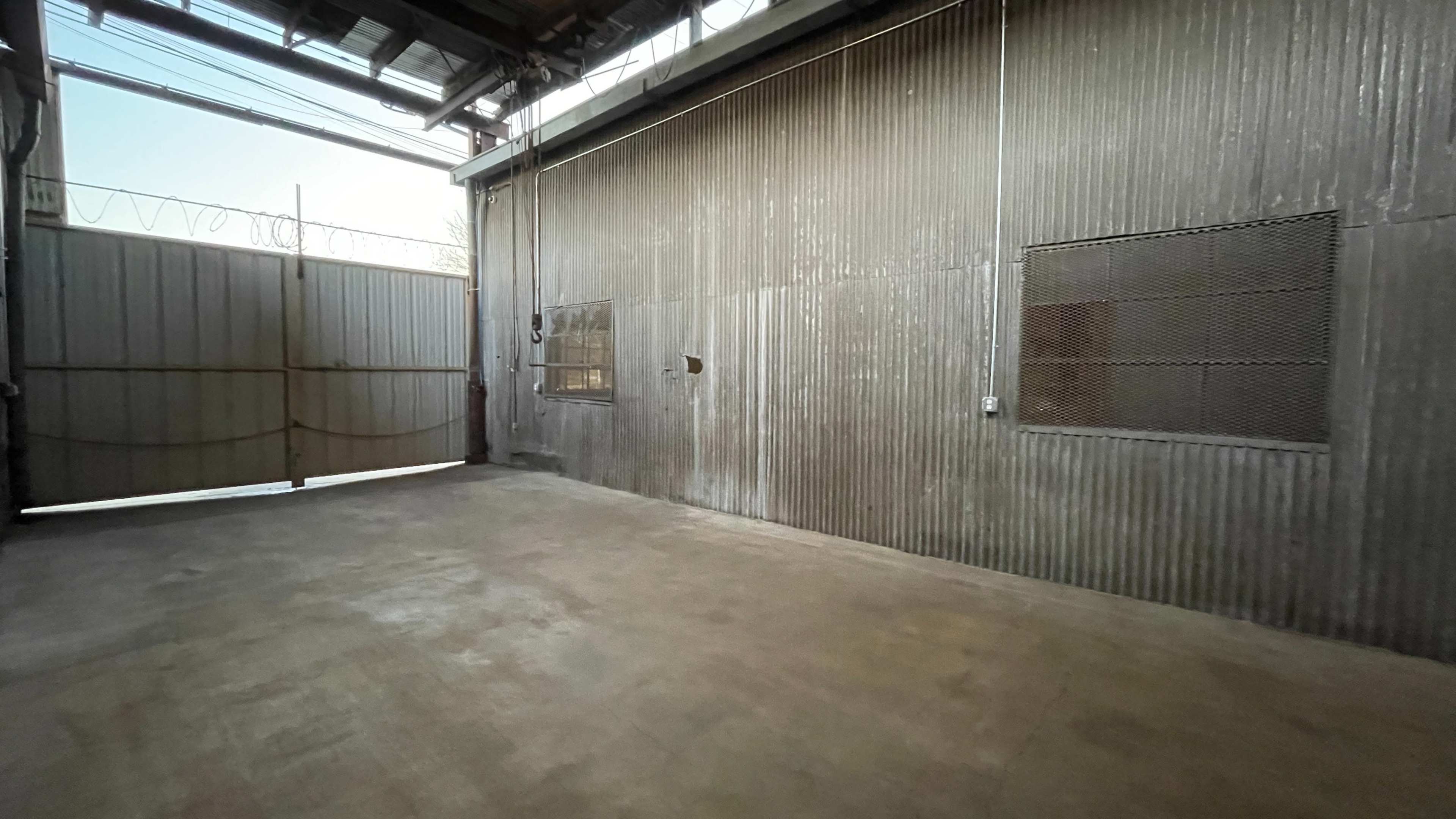 An empty industrial space with a corrugated metal wall and large open gates.
