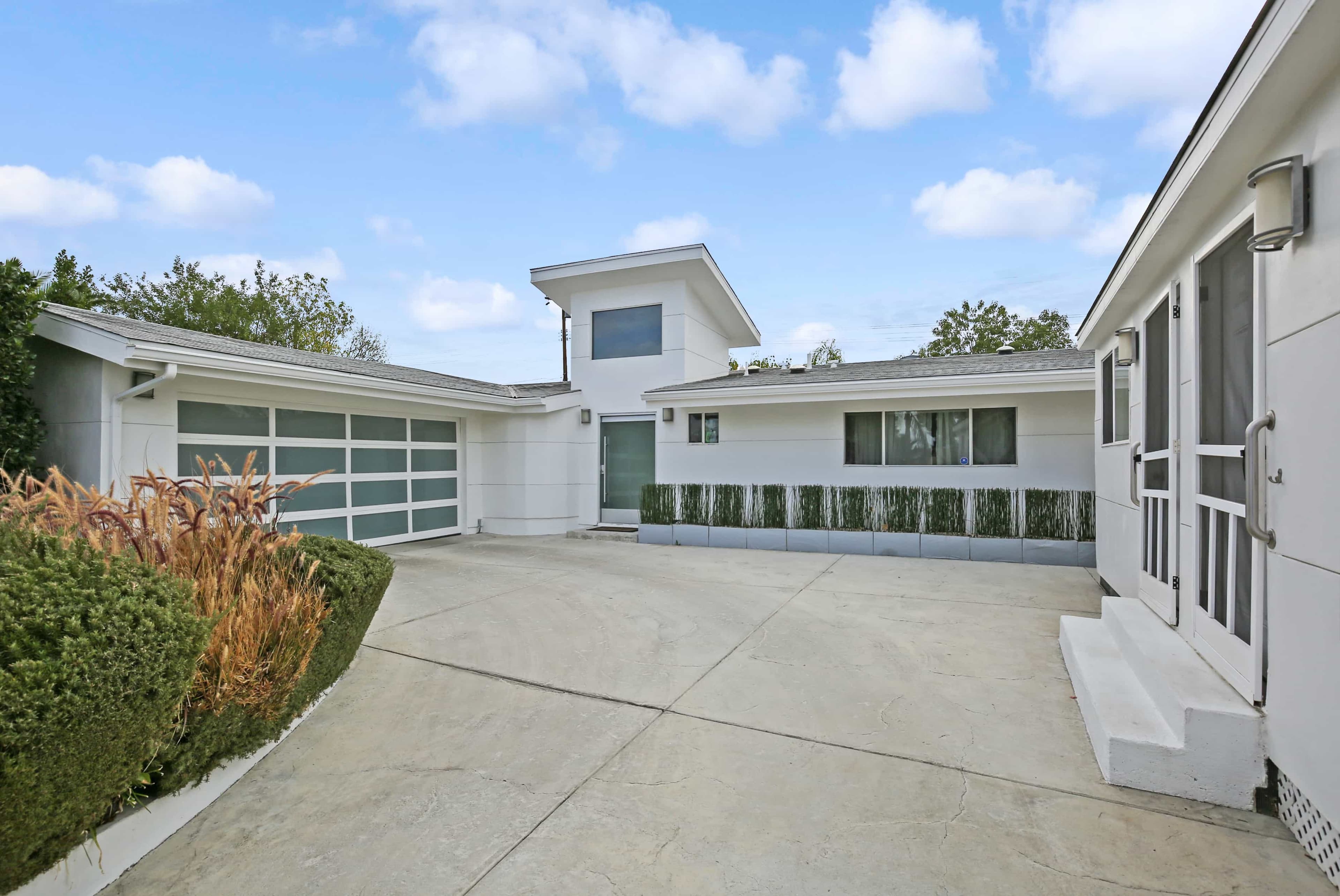 A modern house with a paved driveway, large garage door, and landscaped greenery surrounding the structure.