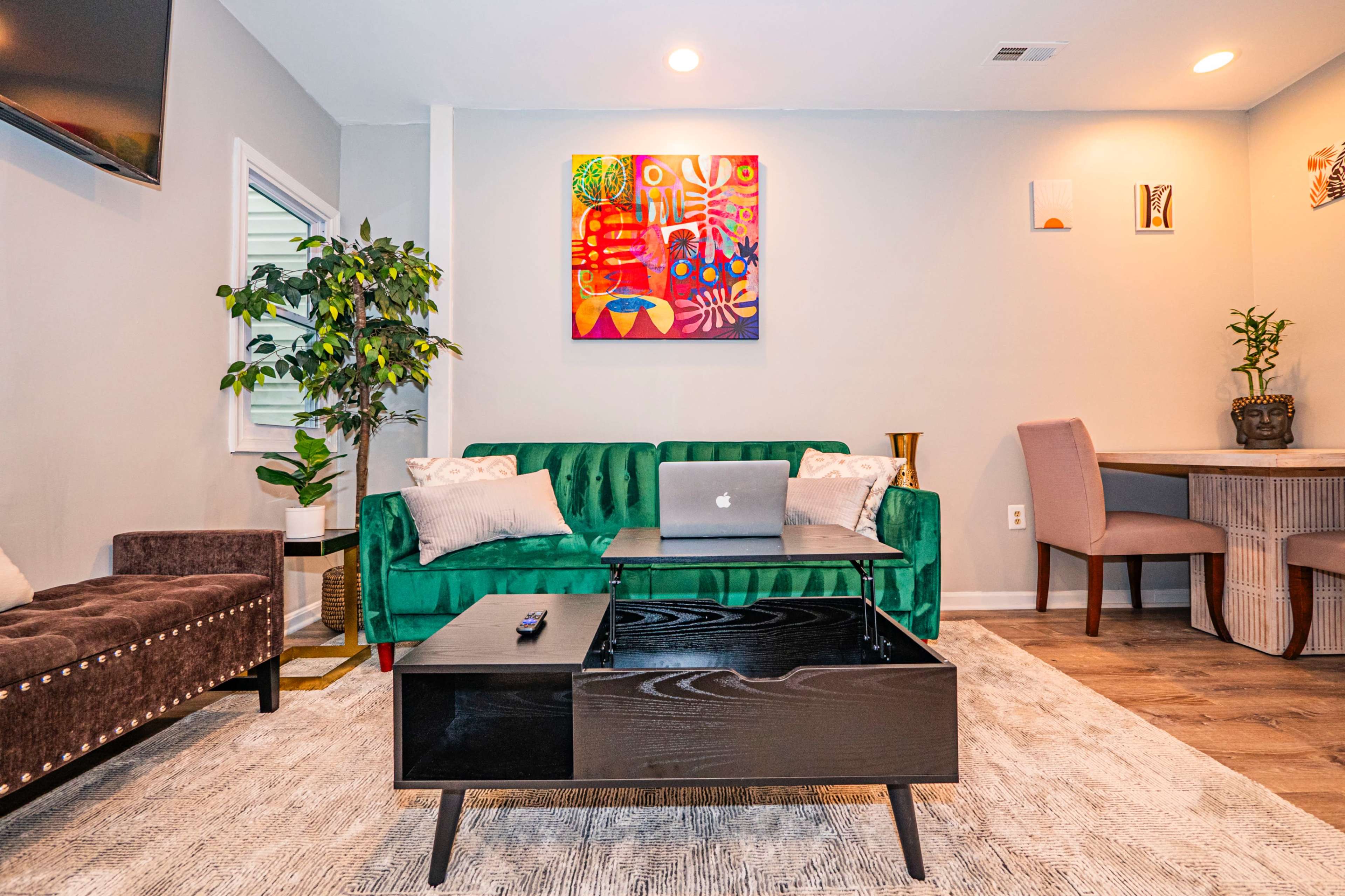 The image shows a modern living room with a green velvet couch, a black coffee table, a wall-mounted television, and a colorful piece of artwork above the couch.