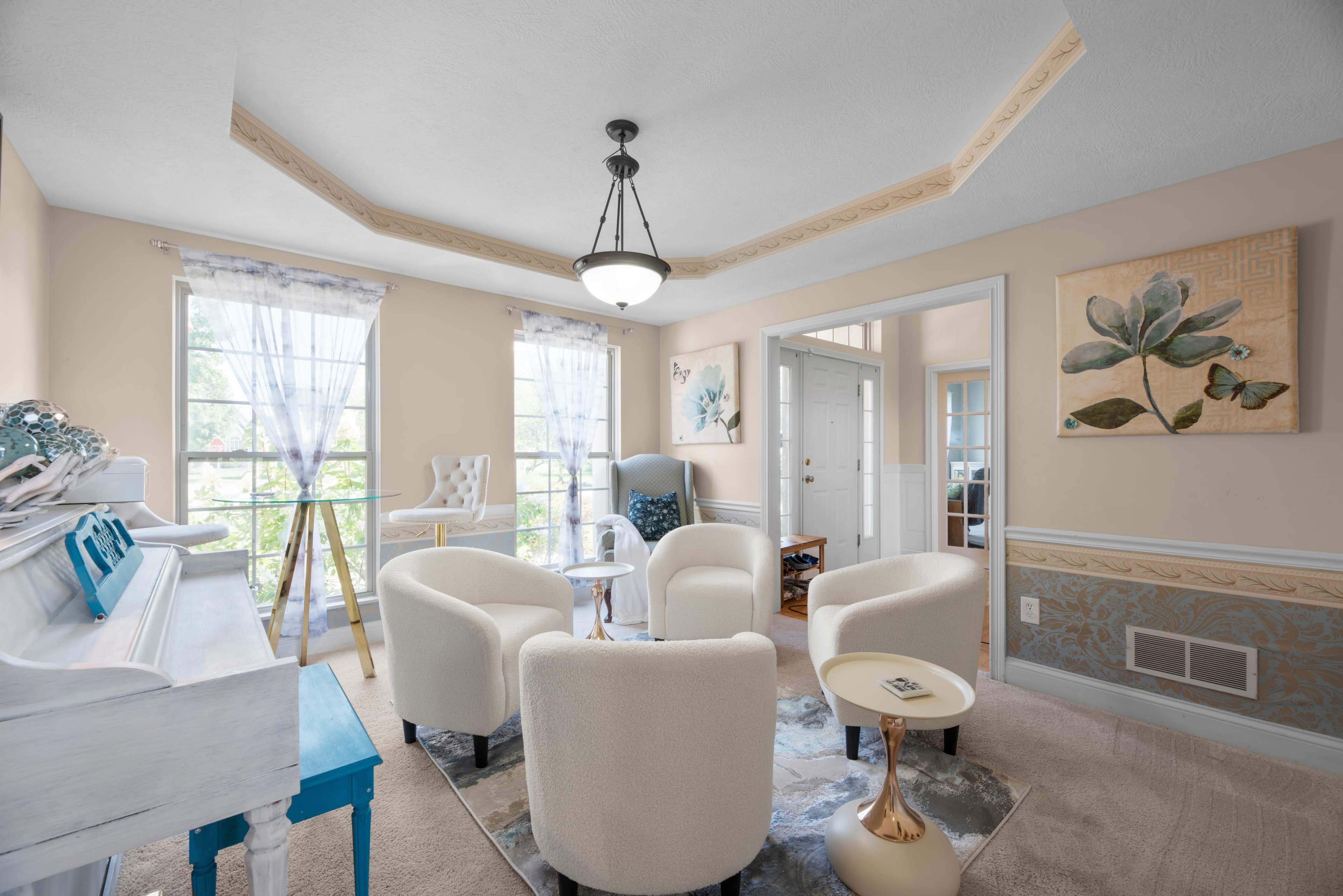 A bright seating area features several cream-colored chairs arranged around a small table, with large windows allowing natural light to illuminate the space.