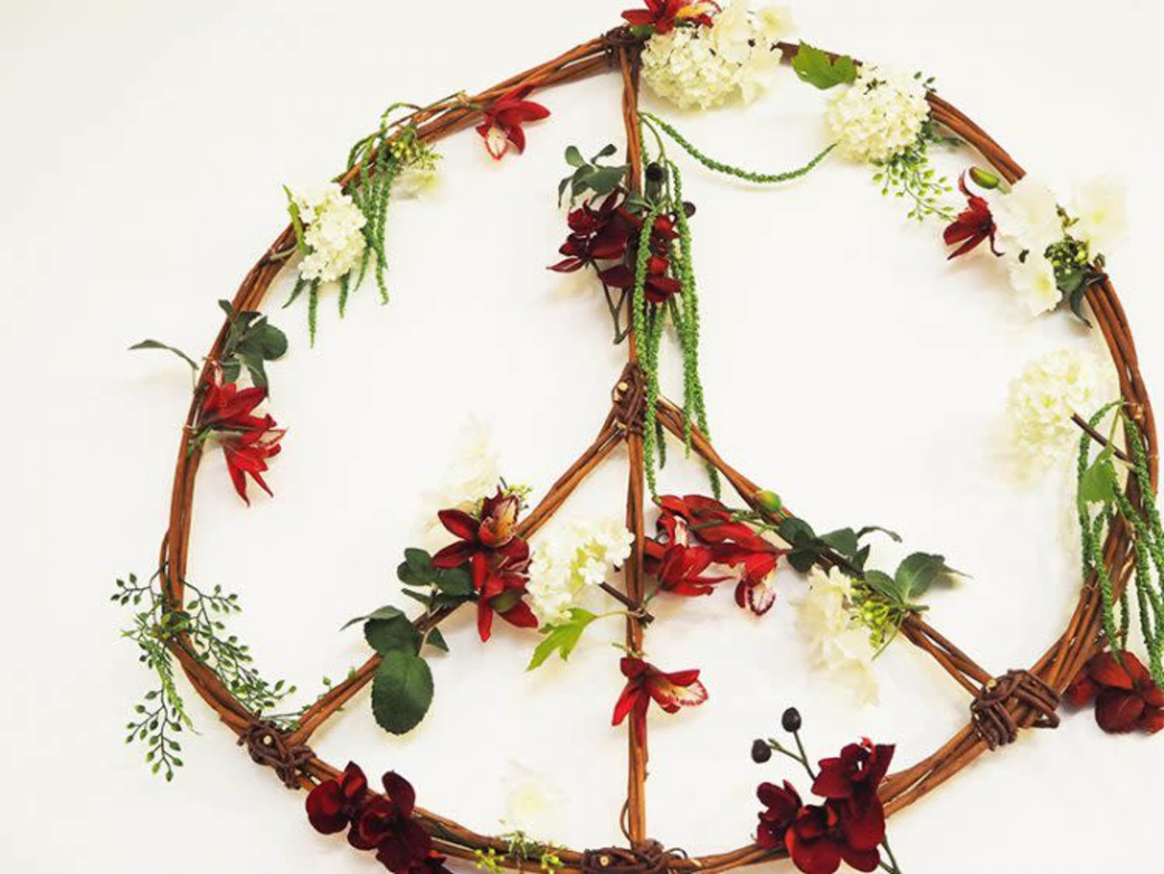 A decorative peace sign made of twigs and adorned with various artificial flowers.
