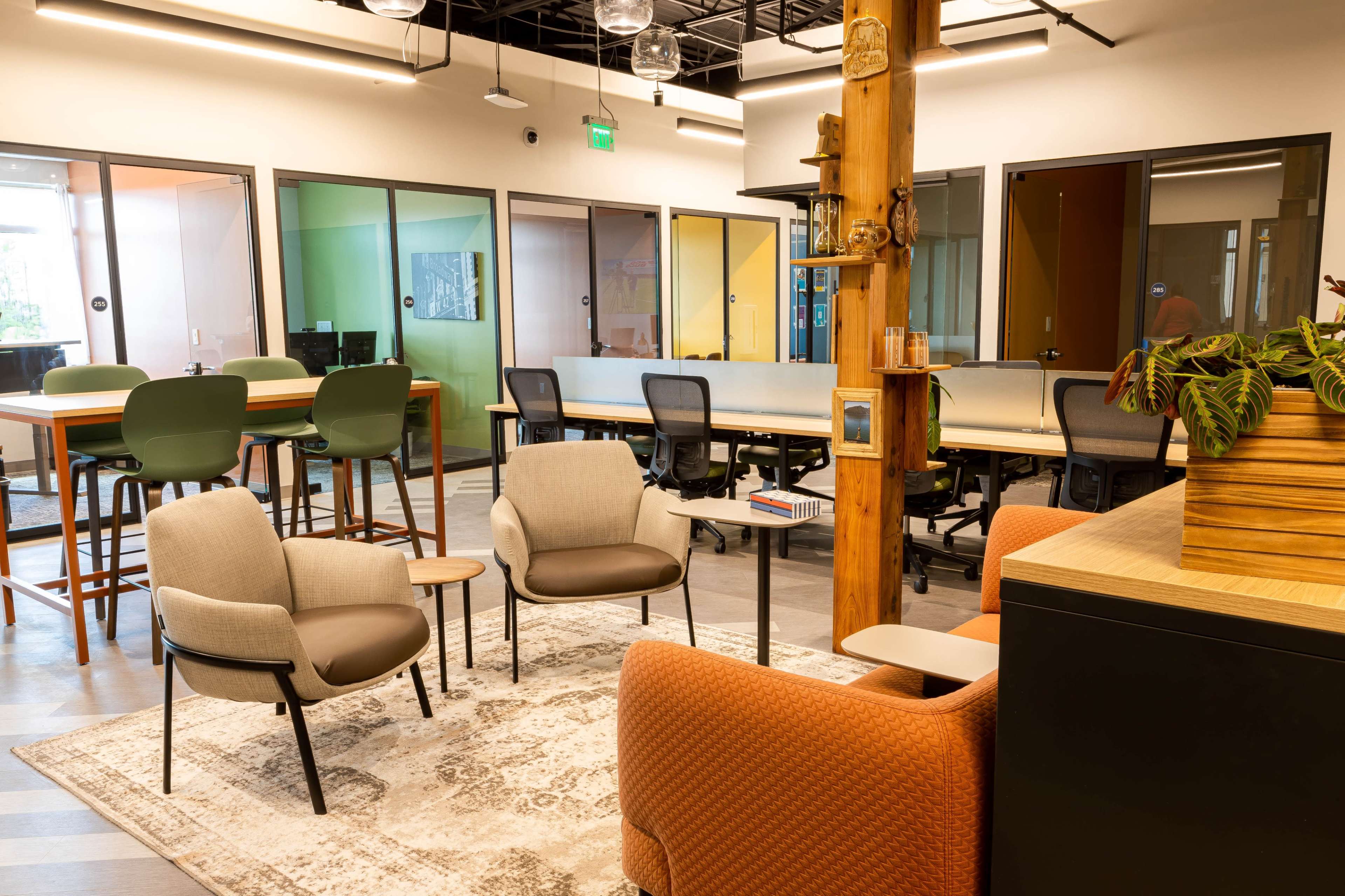 The image shows a modern office space with seating arrangements, workstations, and colorful glass partitions.