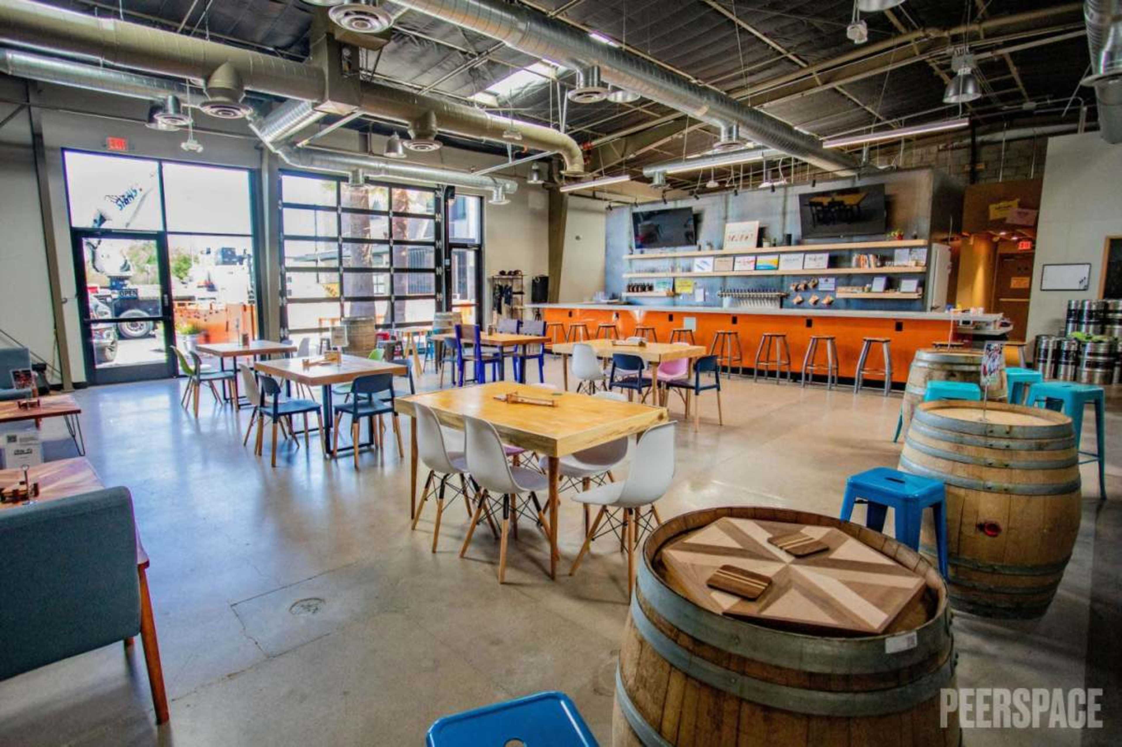The image shows a spacious, modern indoor area with various tables, colorful chairs, and a bar counter along one wall.