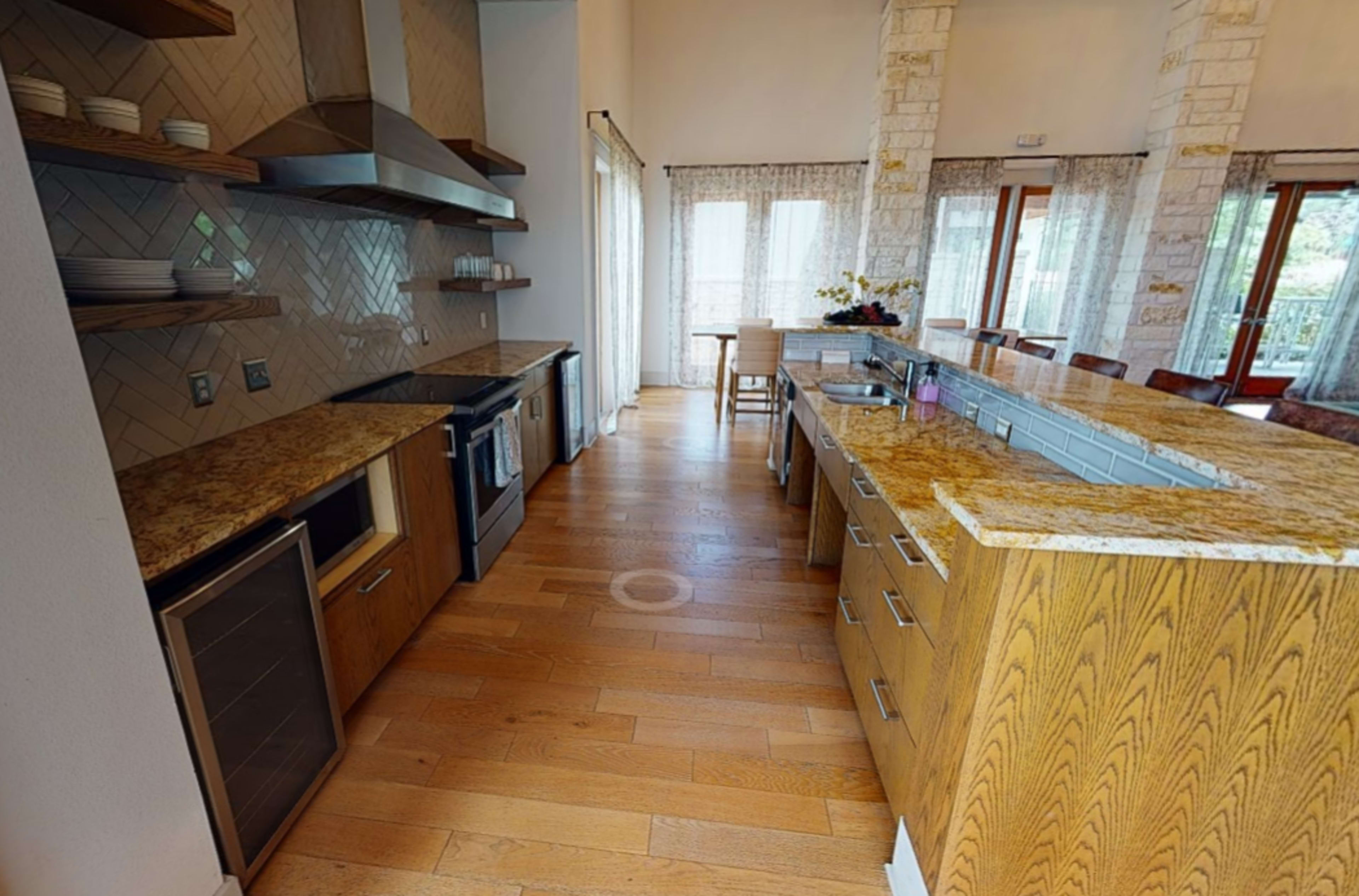 A modern kitchen with wooden cabinets, granite countertops, and large windows allowing natural light to enter.