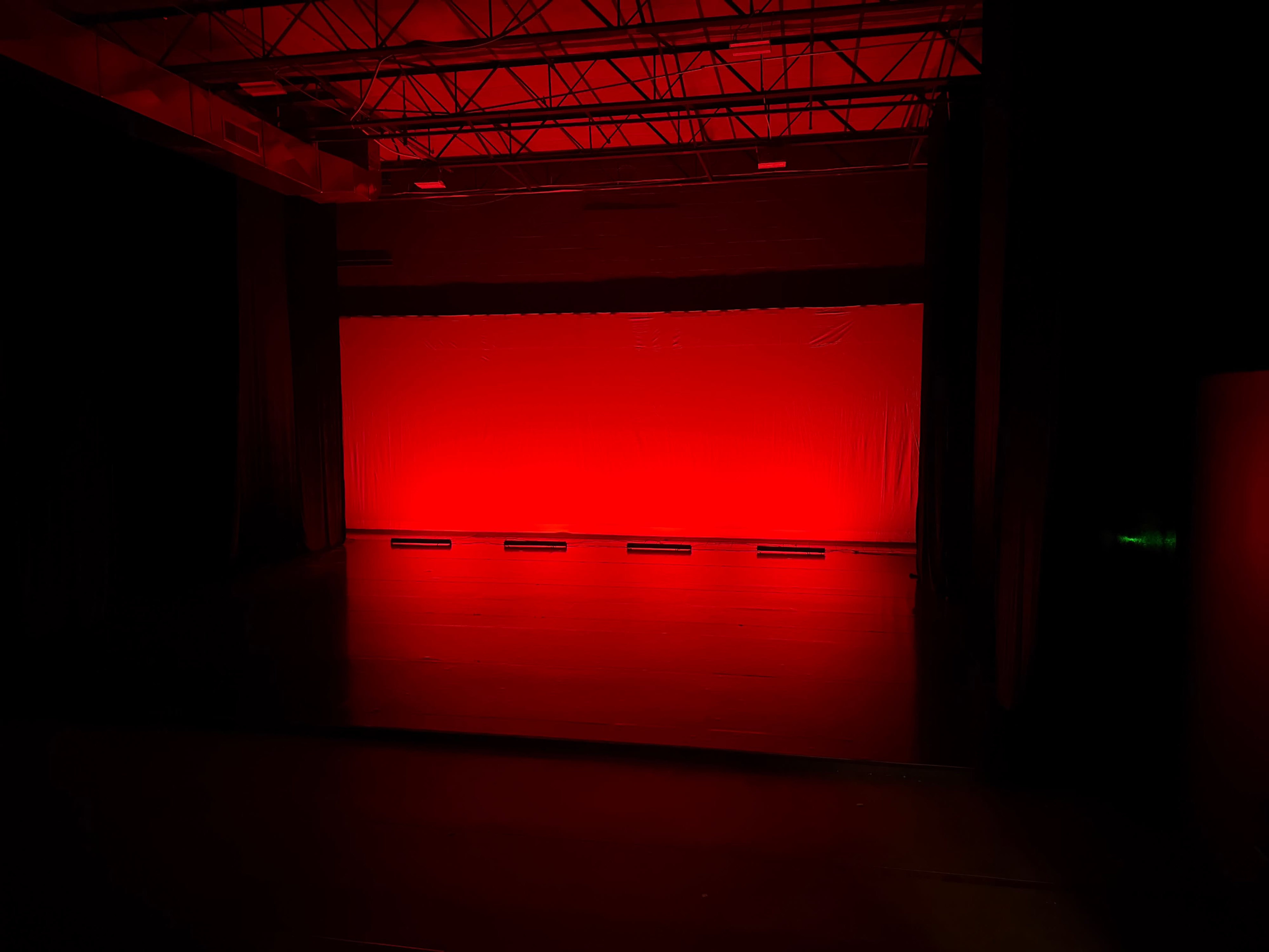 The scene shows a dimly lit stage with a red backdrop and a dark floor, surrounded by black curtains.