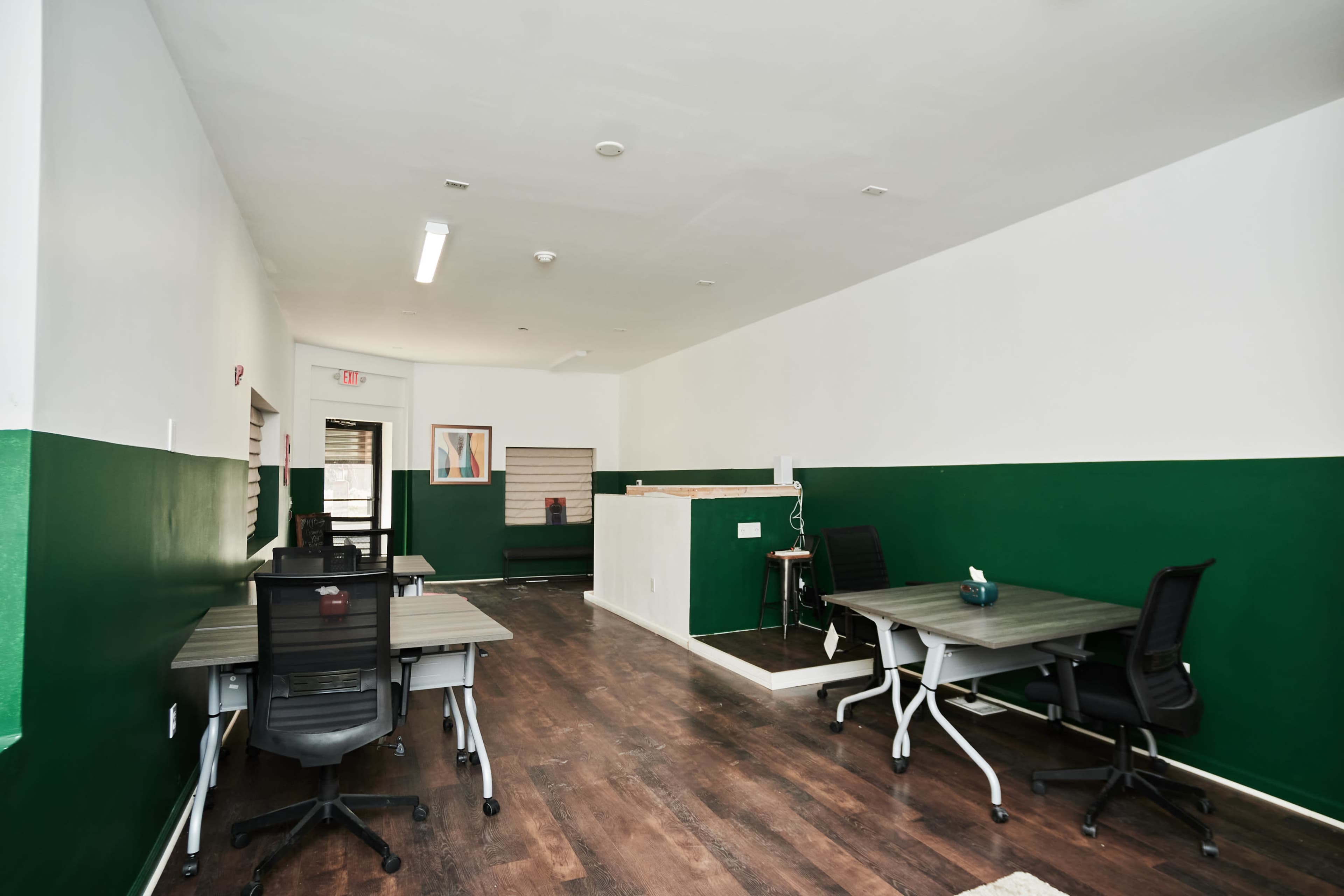 A spacious office interior with green and white walls, featuring several desks arranged in an open layout.