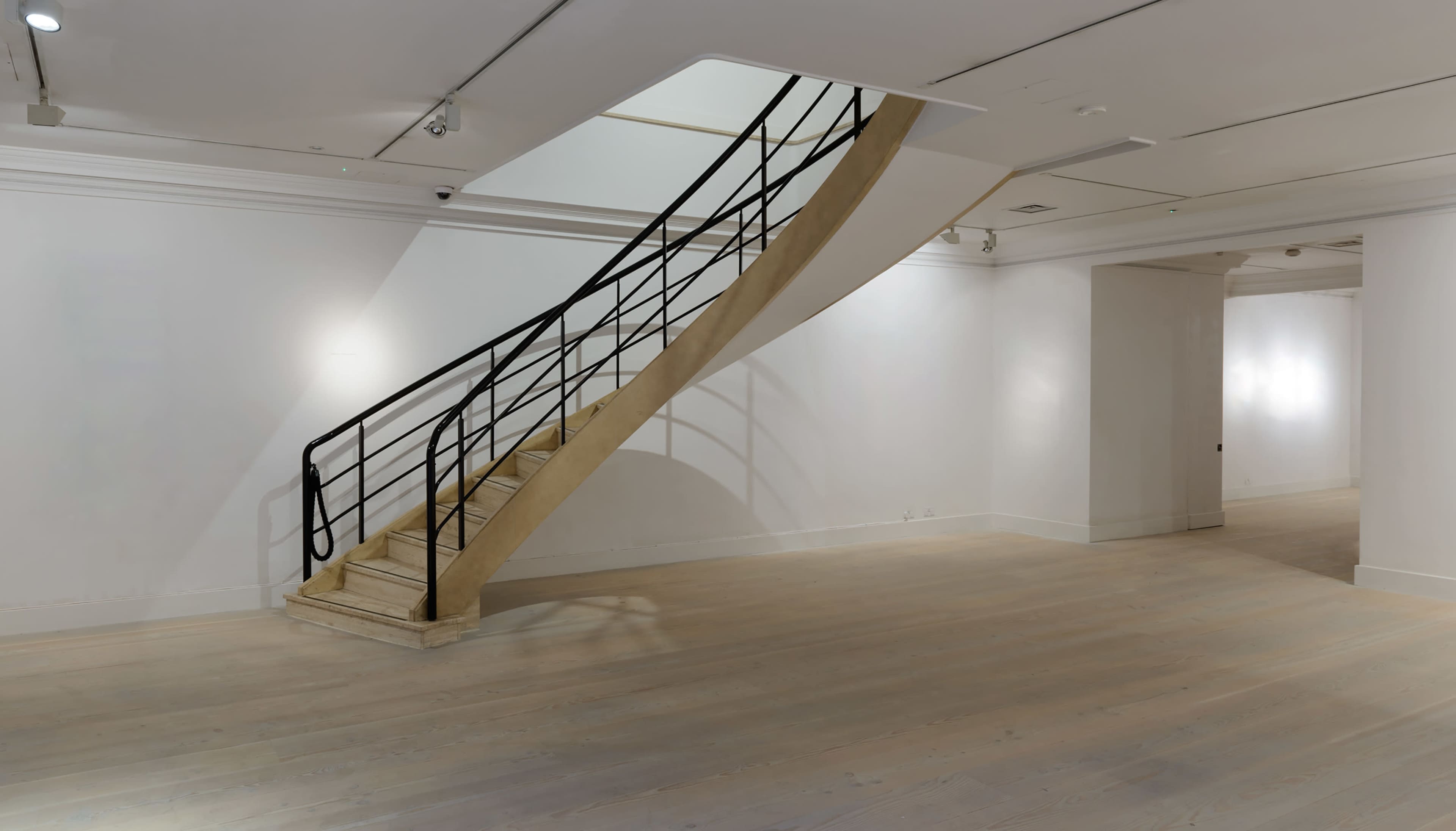 A modern, curved staircase leading to a second level in a minimalist, well-lit room with light wooden flooring.