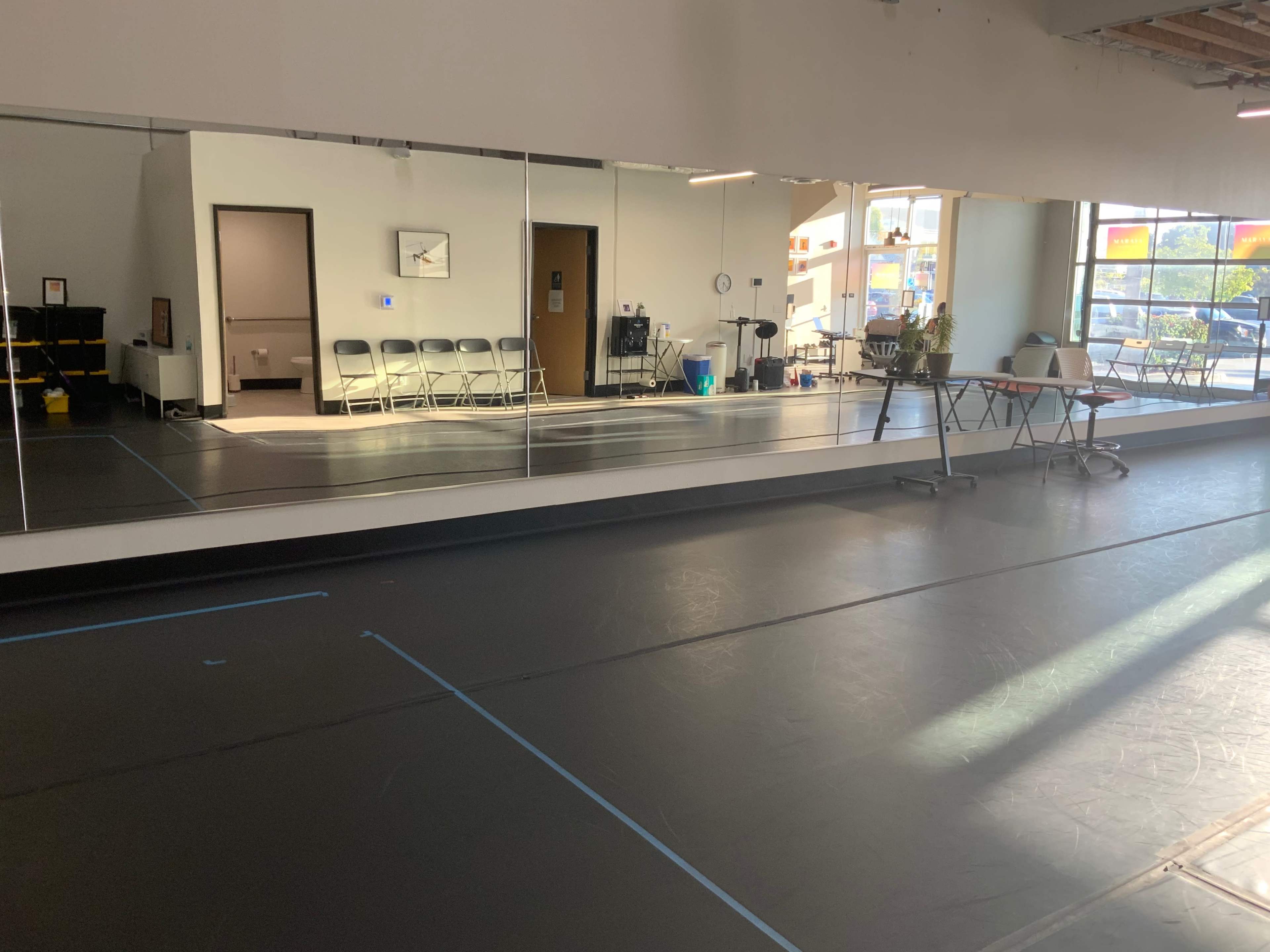 A spacious dance studio with mirrors along one wall, a smooth black floor, and several folding chairs arranged in the background.