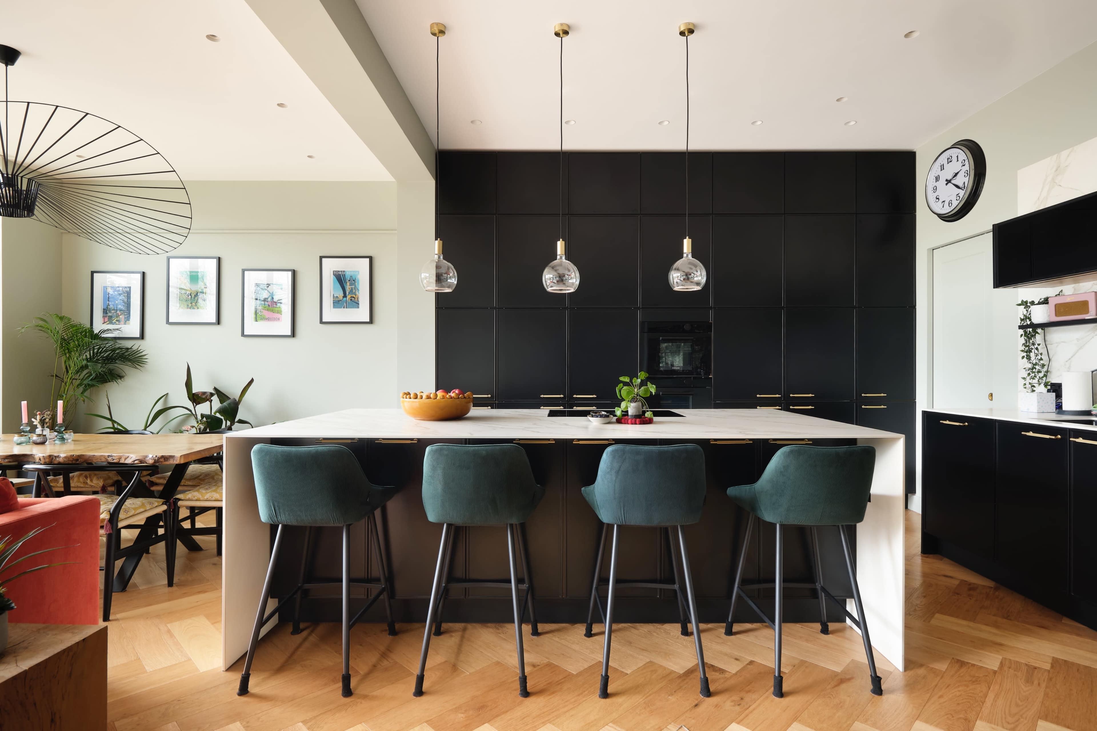 A modern kitchen features a central island with bar stools, dark cabinetry, and geometric lighting.
