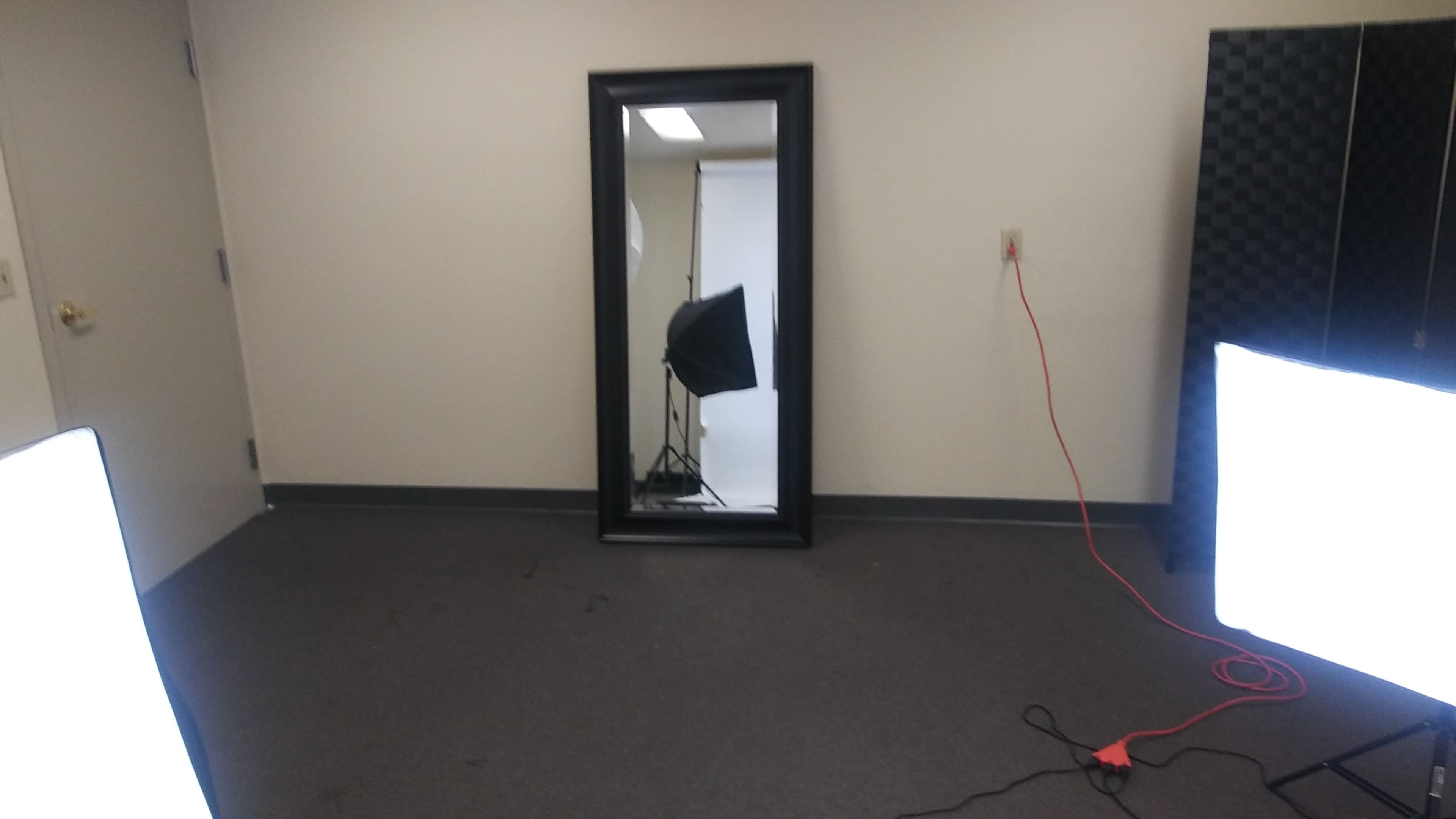 A room with a large mirror, two bright light sources, and a backdrop stand in front of a white wall.