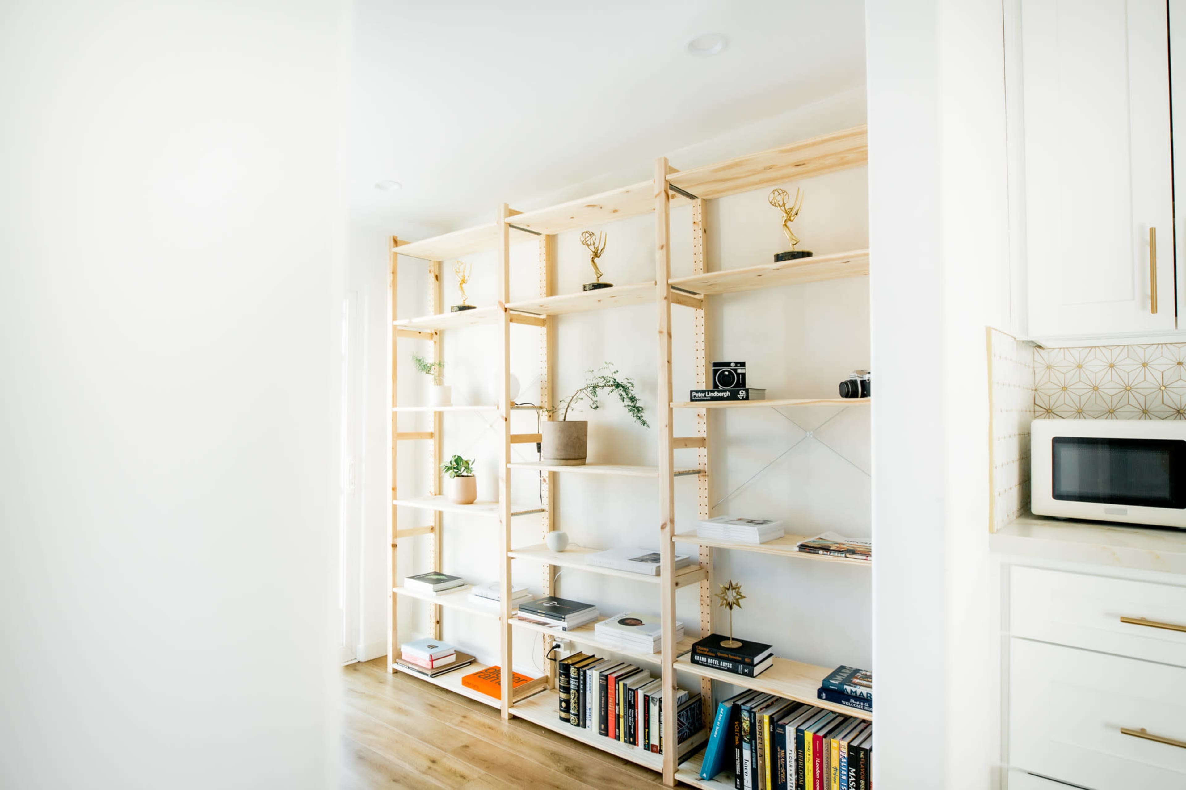 The image shows a wooden bookshelf with various plants, books, and decorative items in a well-lit room.