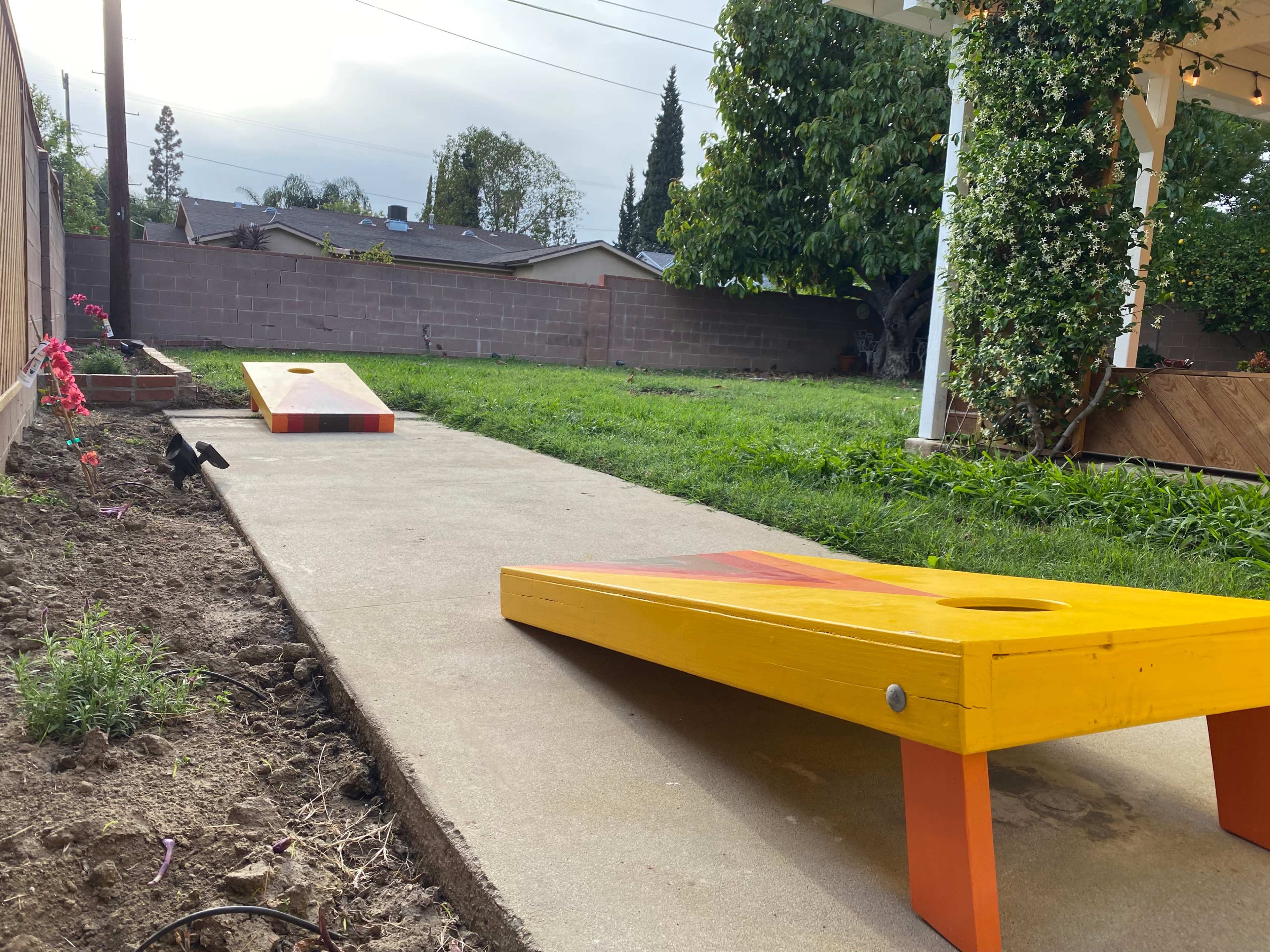 A concrete pathway leading to two yellow bean bag toss boards in a residential backyard.
