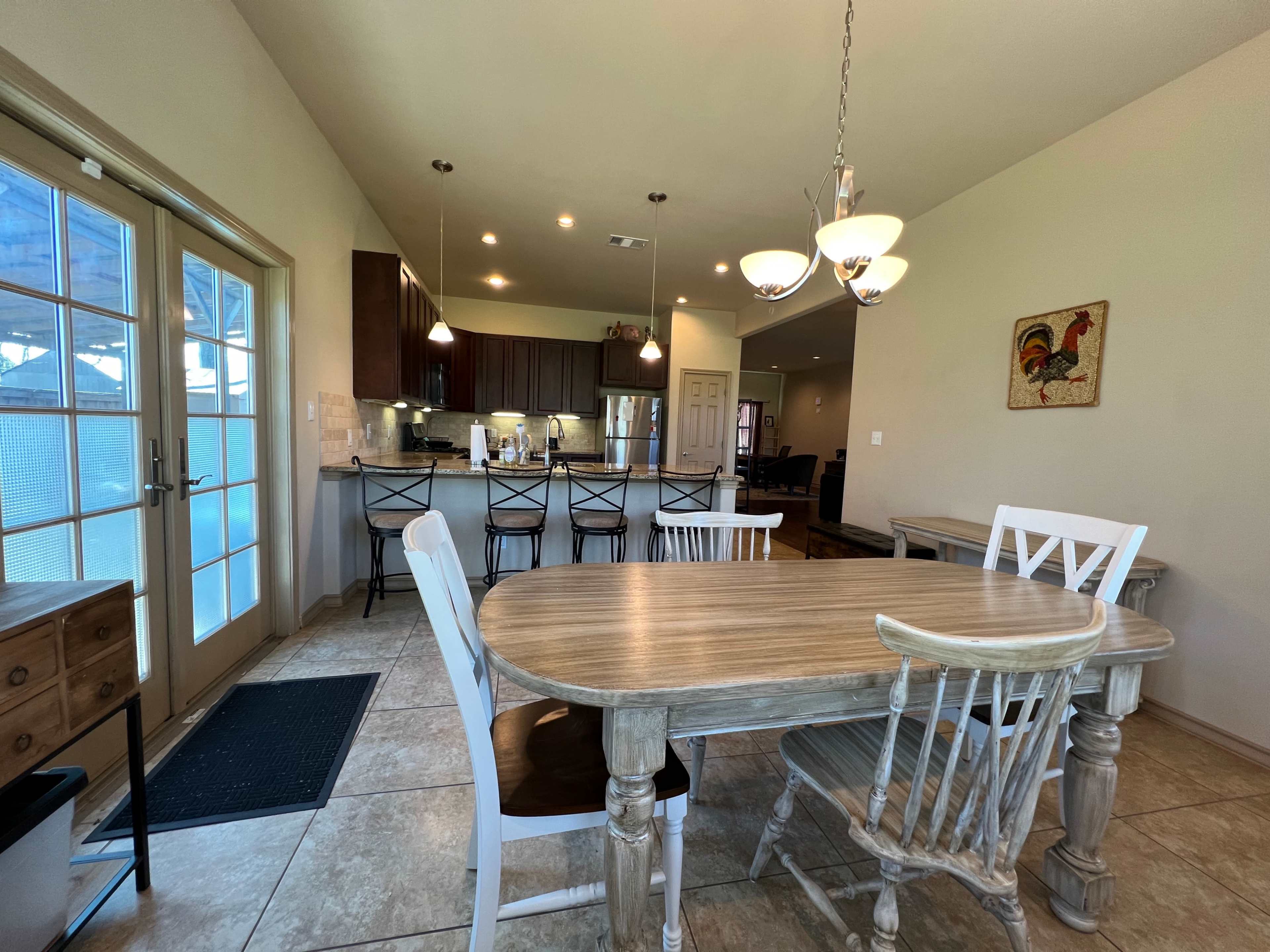 A dining area features a round wooden table surrounded by chairs, with a view of a modern kitchen in the background.