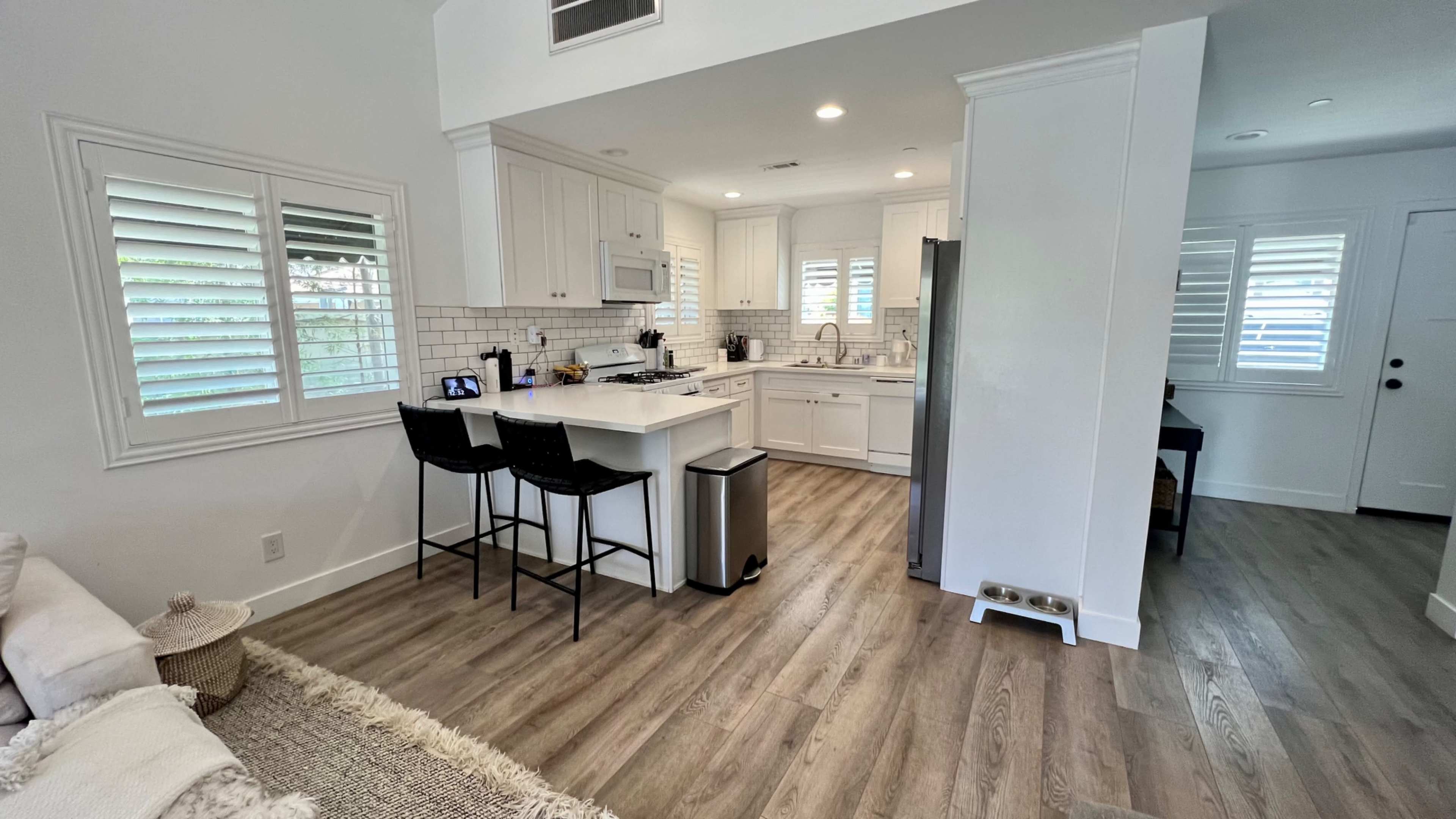 A bright, modern kitchen and dining area with white cabinets, stainless steel appliances, and bar seating.