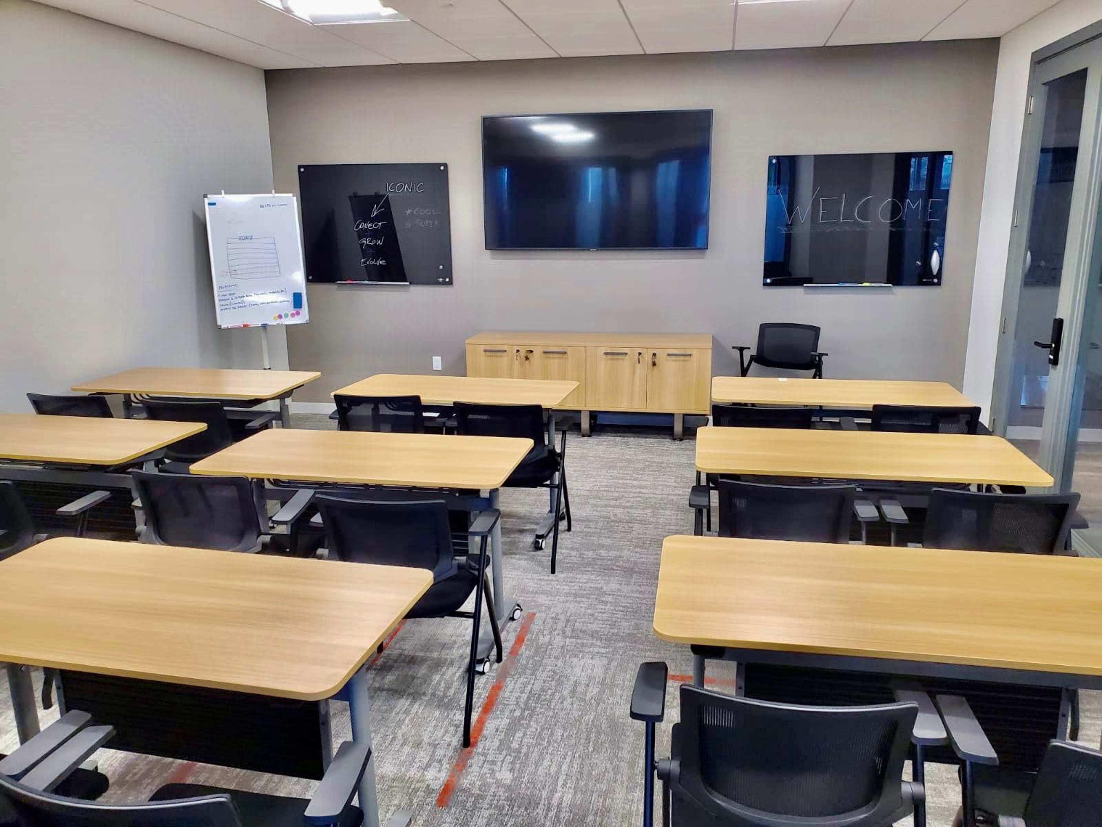 A modern classroom equipped with desks, chairs, and two large screens on the walls.