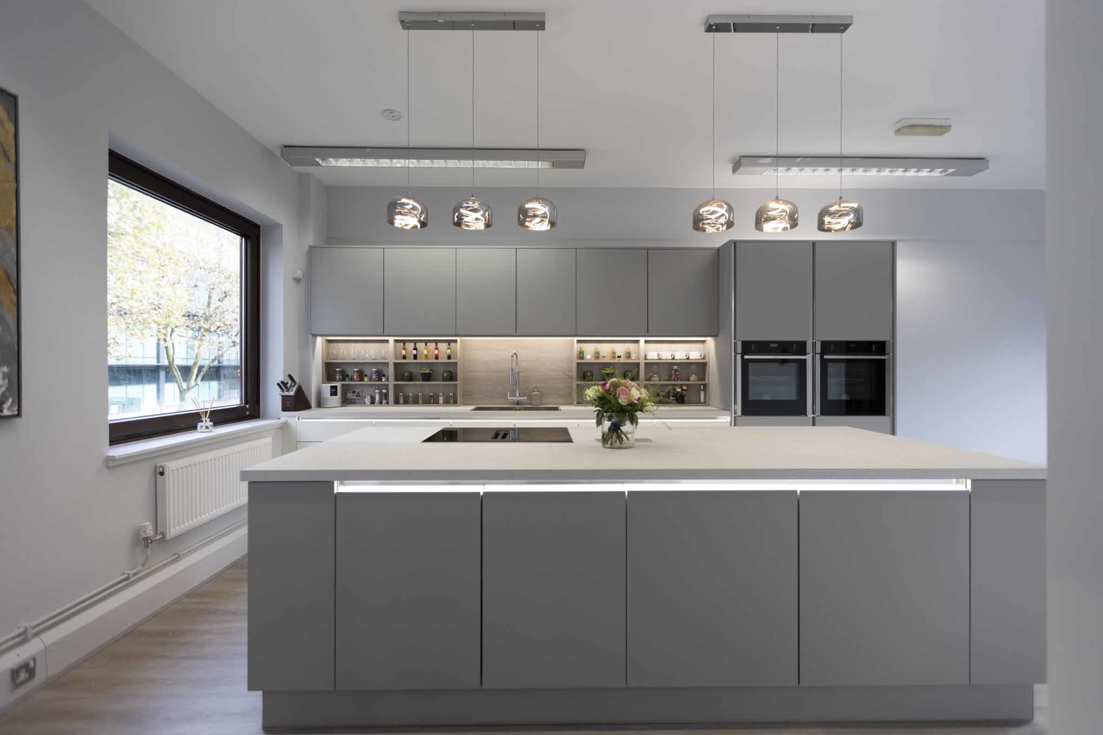 A modern kitchen with a large central island, gray cabinetry, and pendant lighting above.