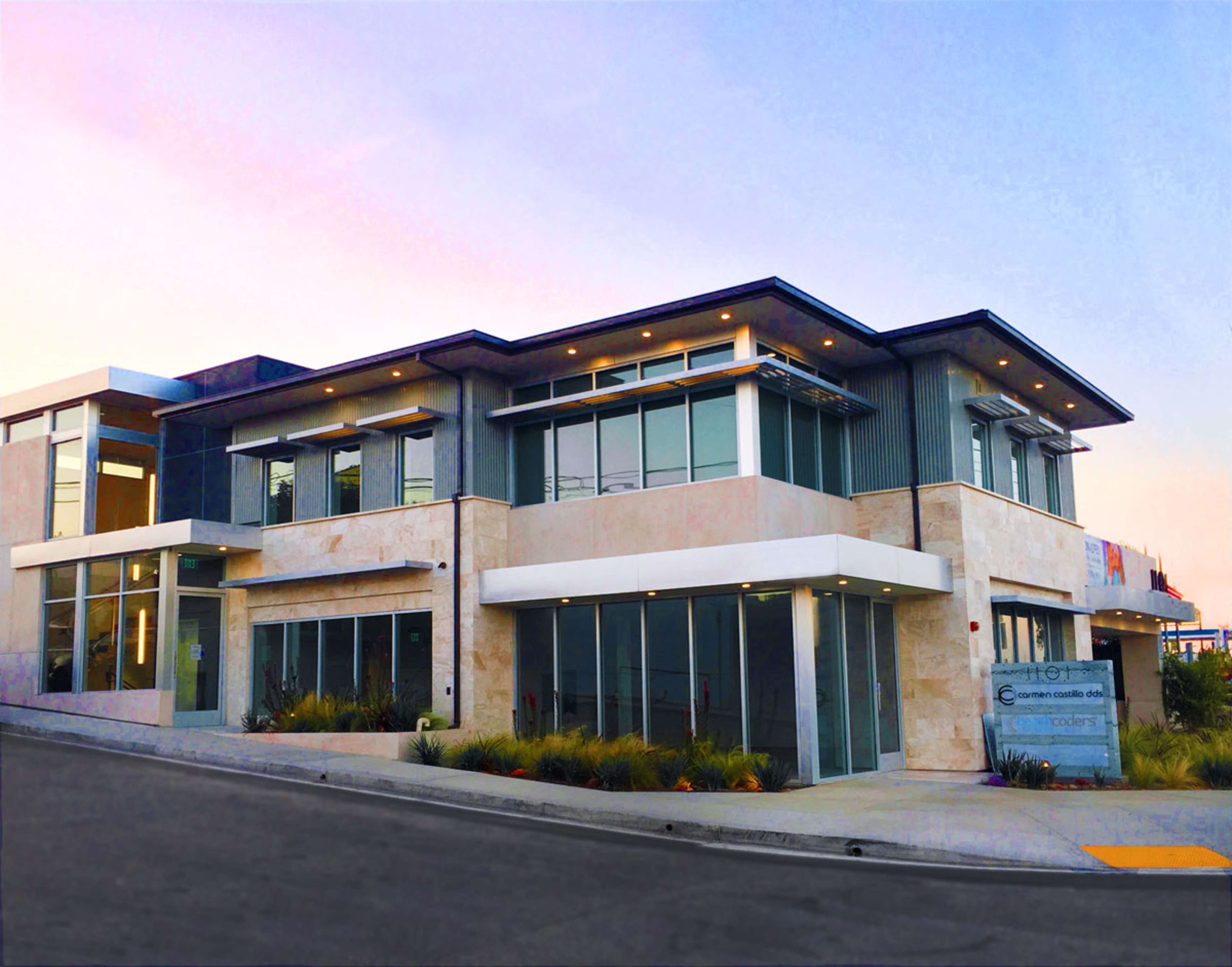 A modern, two-story building with large windows and a smooth facade, situated at the corner of a street.