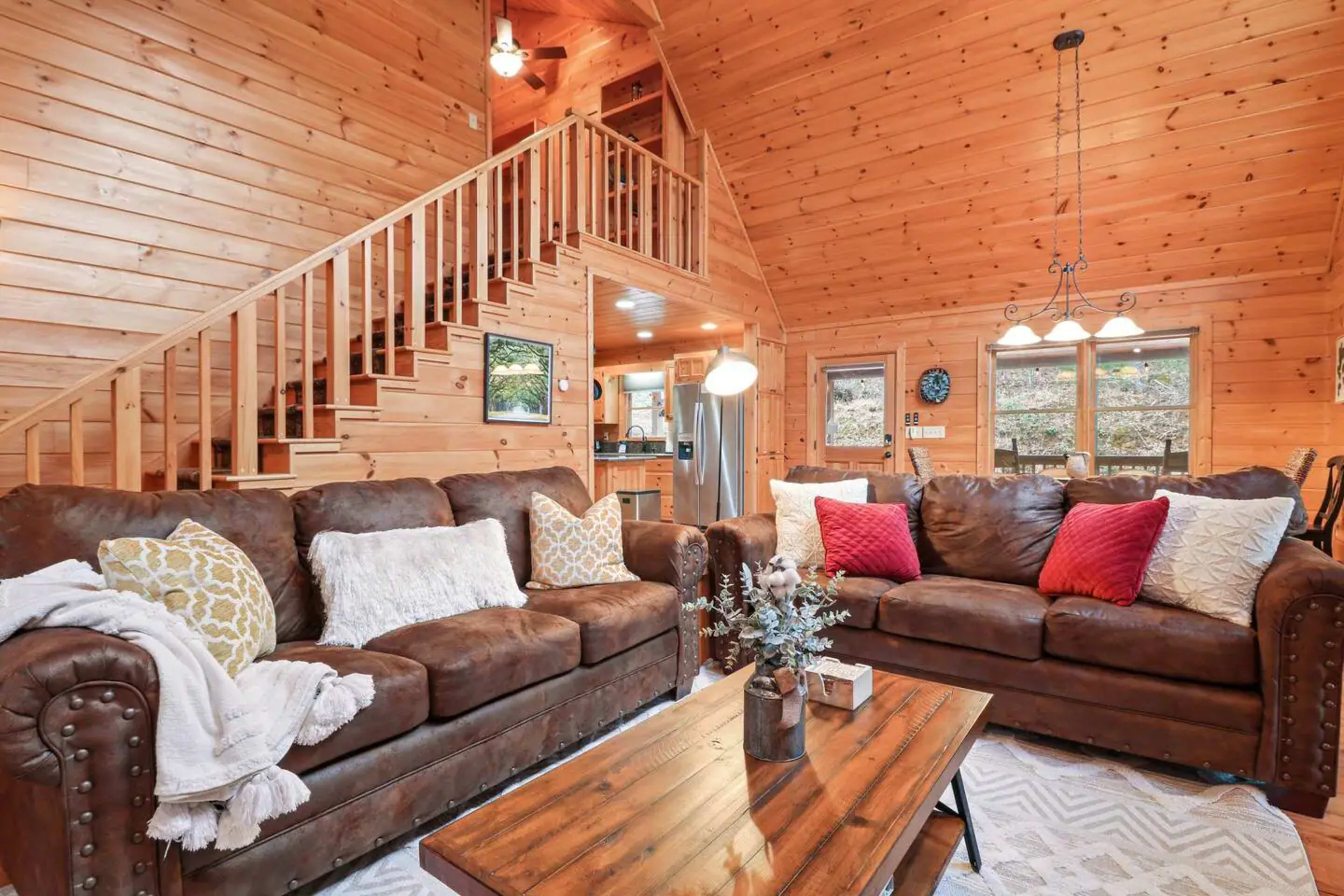 A wooden interior living room with two brown sofas, a coffee table, and a staircase leading to an upper level.