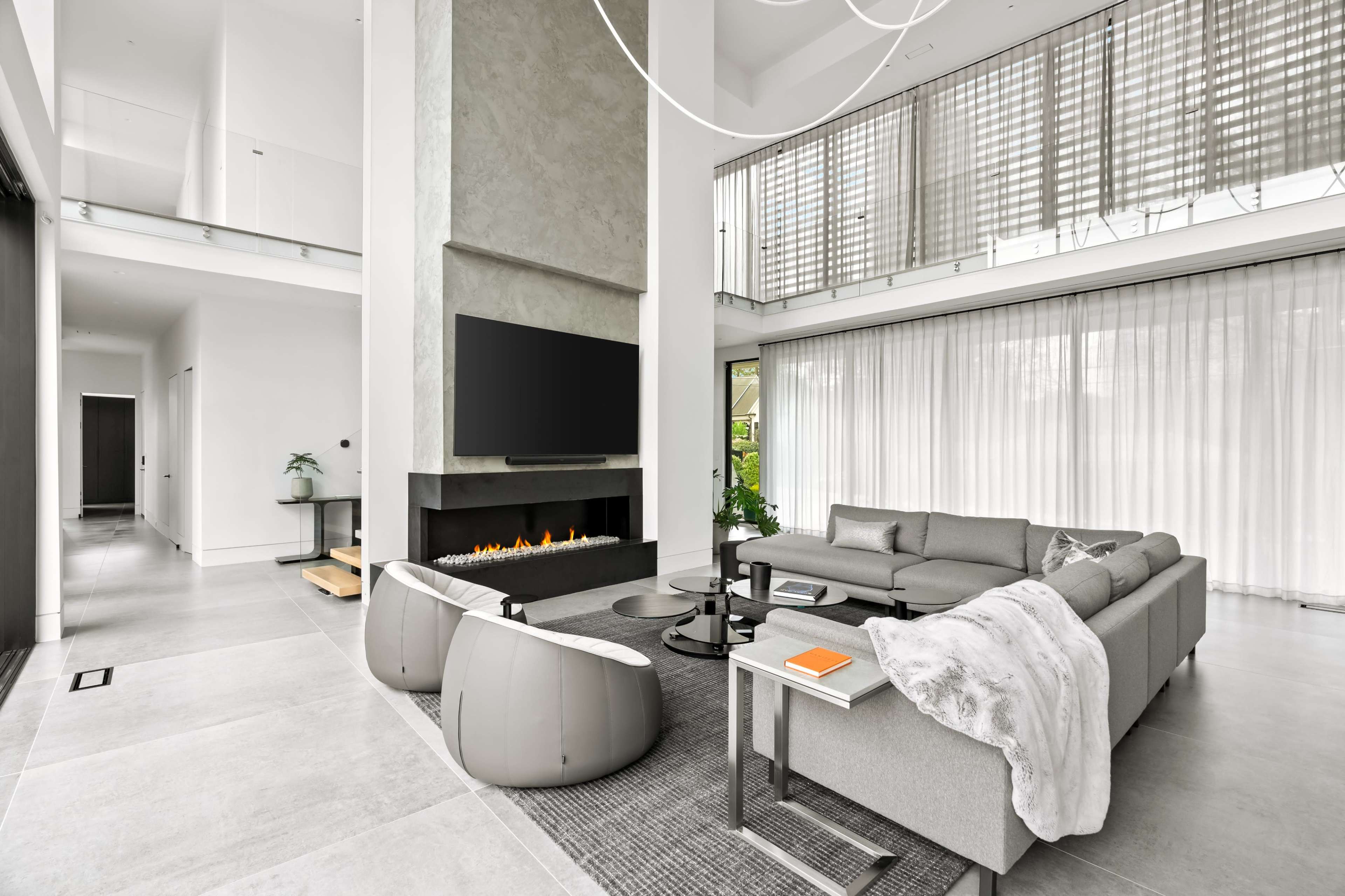 The image features a modern living room with a large sectional sofa, a minimalist fireplace, and floor-to-ceiling windows that allow natural light to enter.