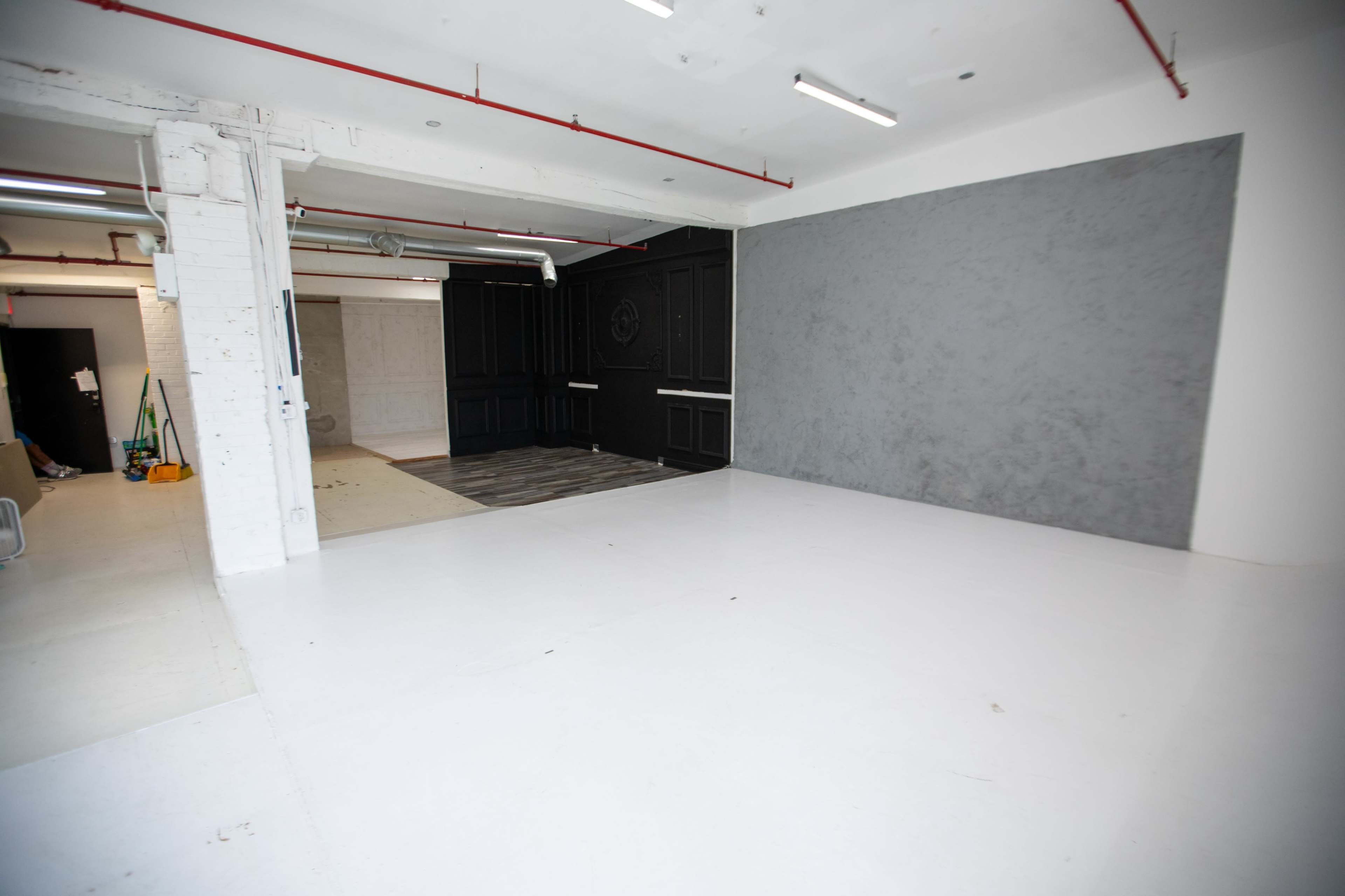 The image shows an interior space with a white floor, a gray wall, and an adjacent dark-colored paneling area, along with cleaning supplies in the corner.