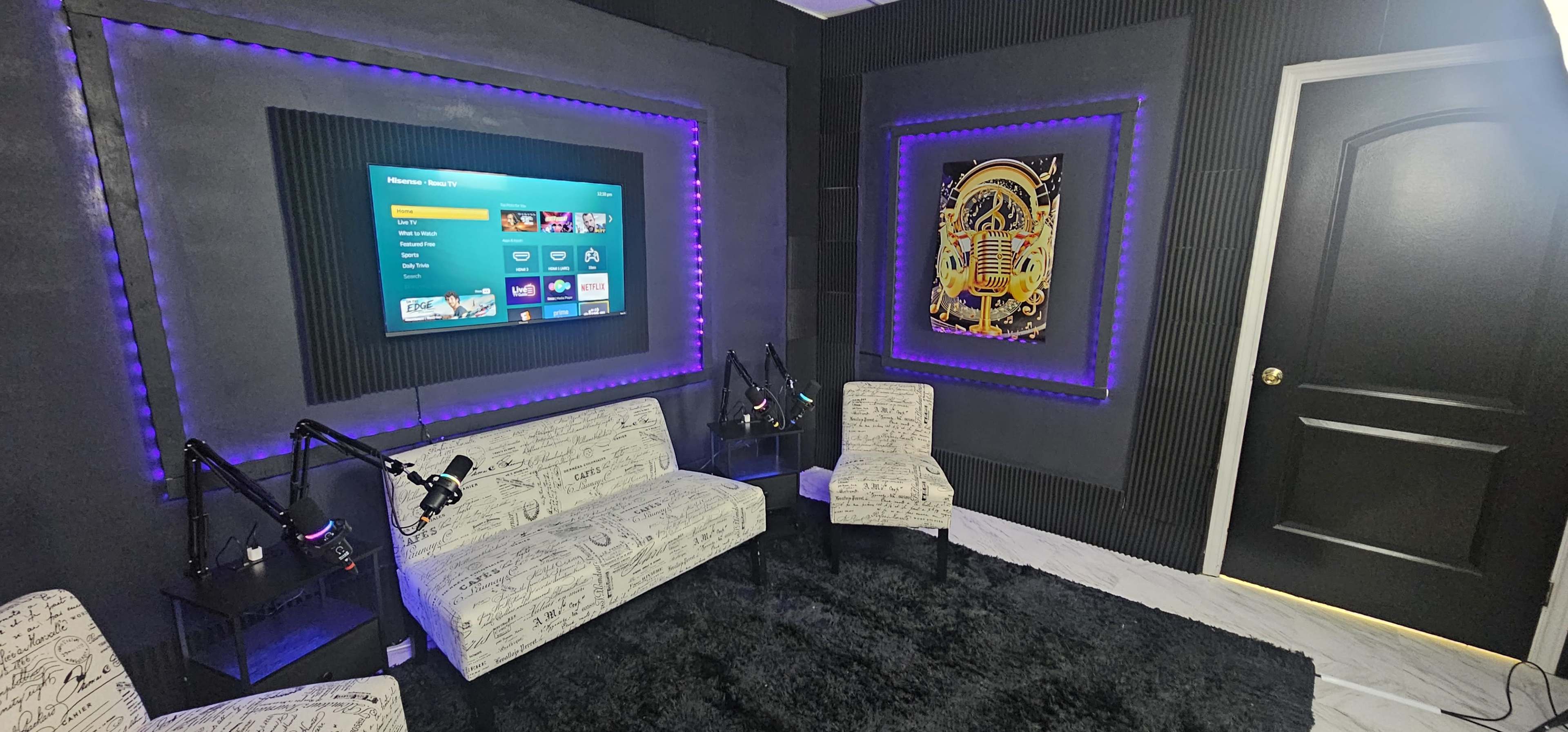 The image shows a modern room with a black and purple color scheme, featuring two light-colored sofas, a television mounted on the wall, and an art piece beside a closed door.