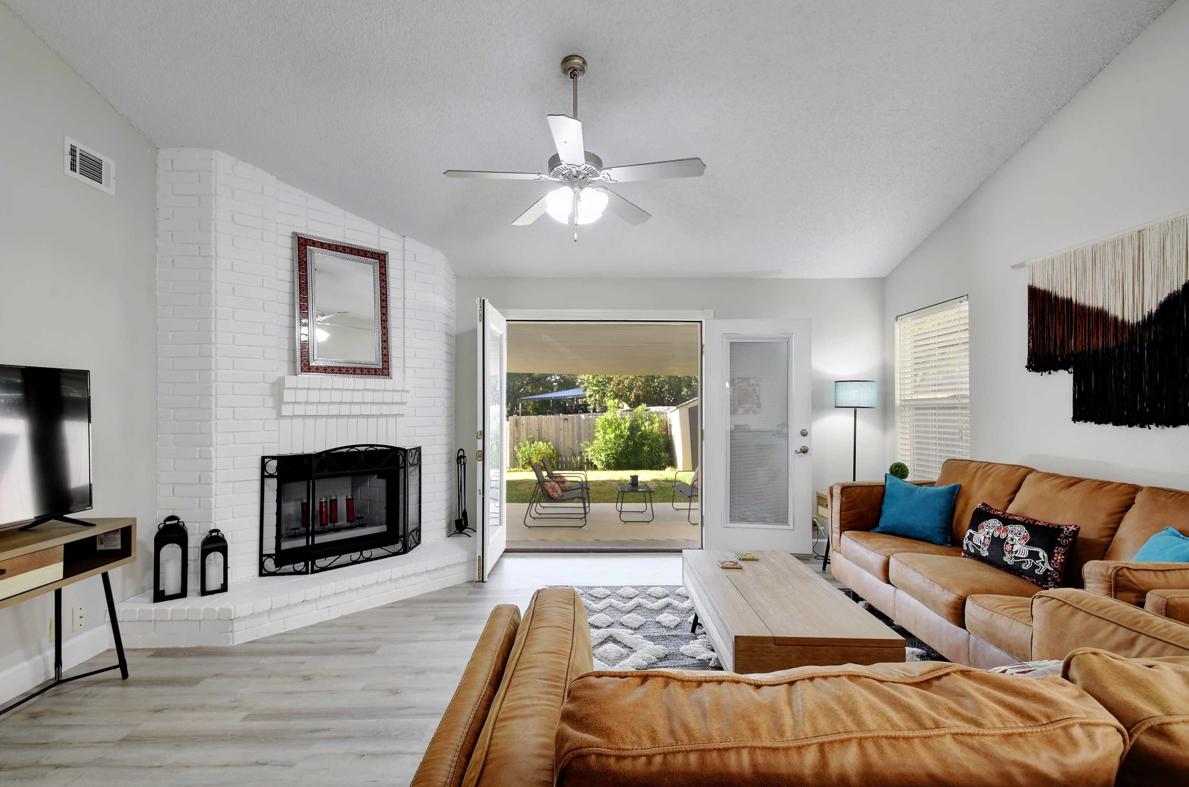 A living room features a fireplace, a large window with a patio view, and two couches arranged around a coffee table.