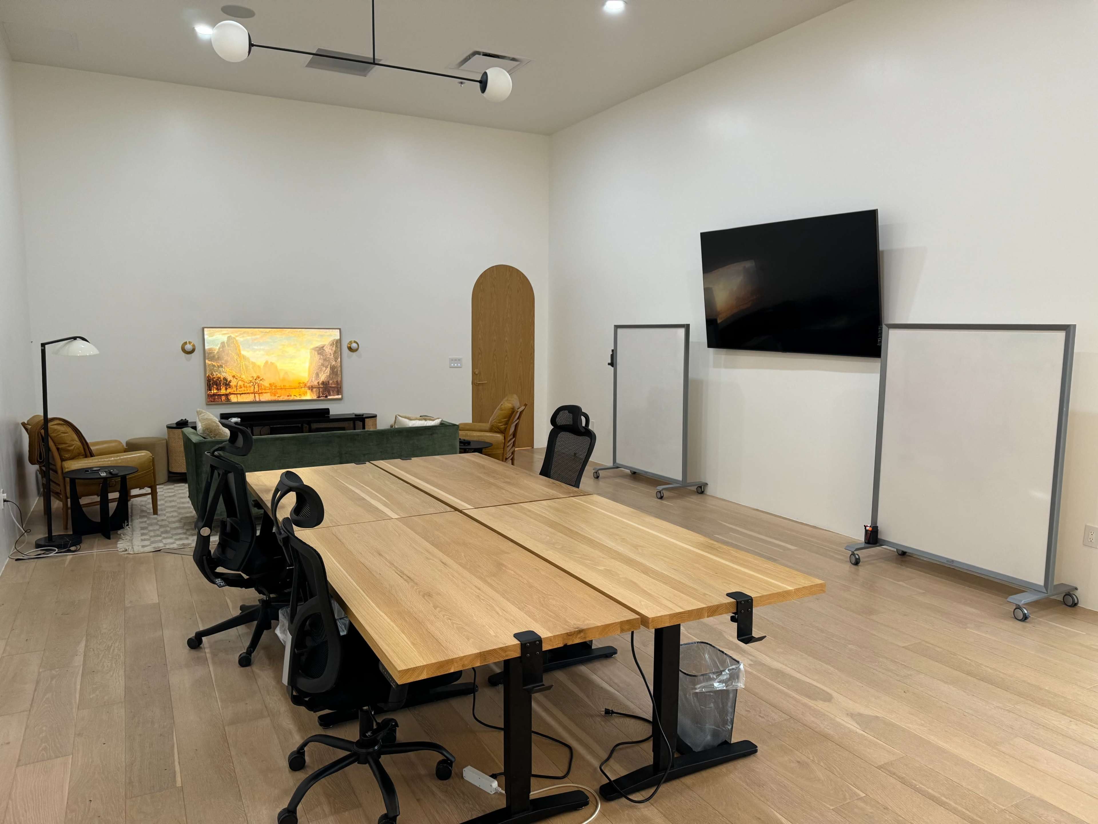 A spacious meeting room with two large tables, several chairs, a television on the wall, and two whiteboards on either side.