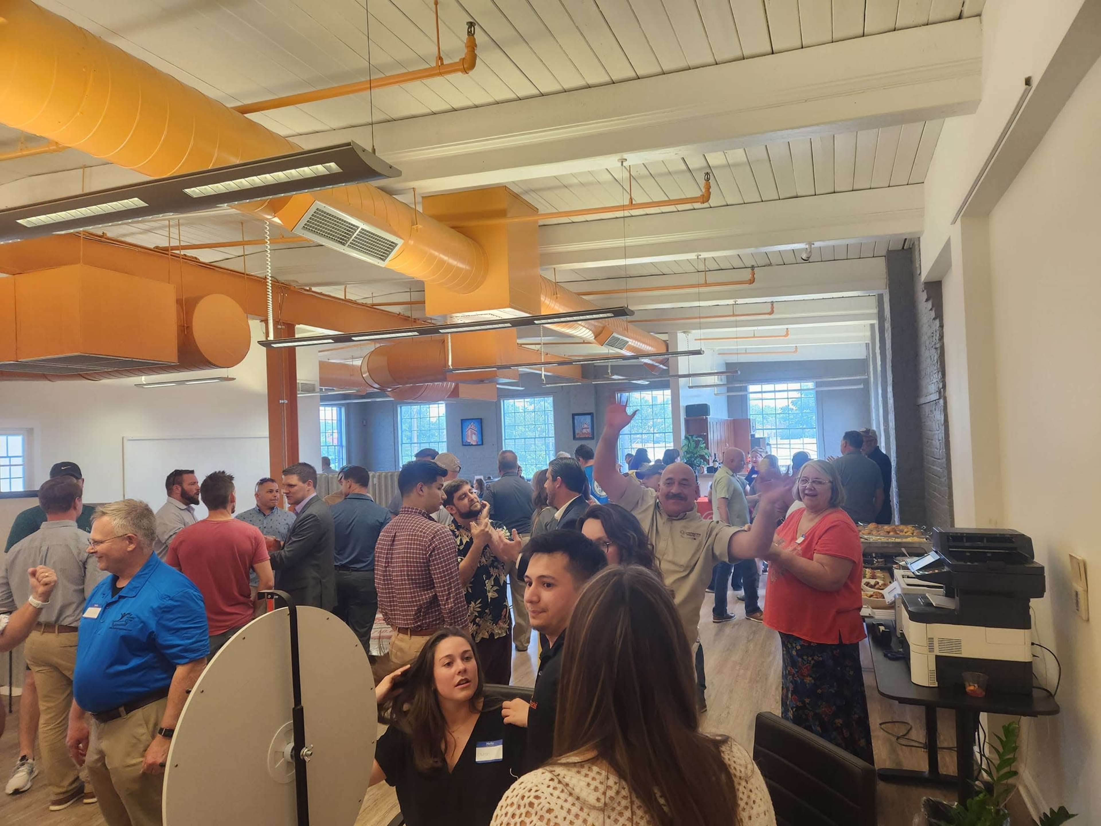 A crowded room filled with people socializing at a networking event, surrounded by orange and white decor.