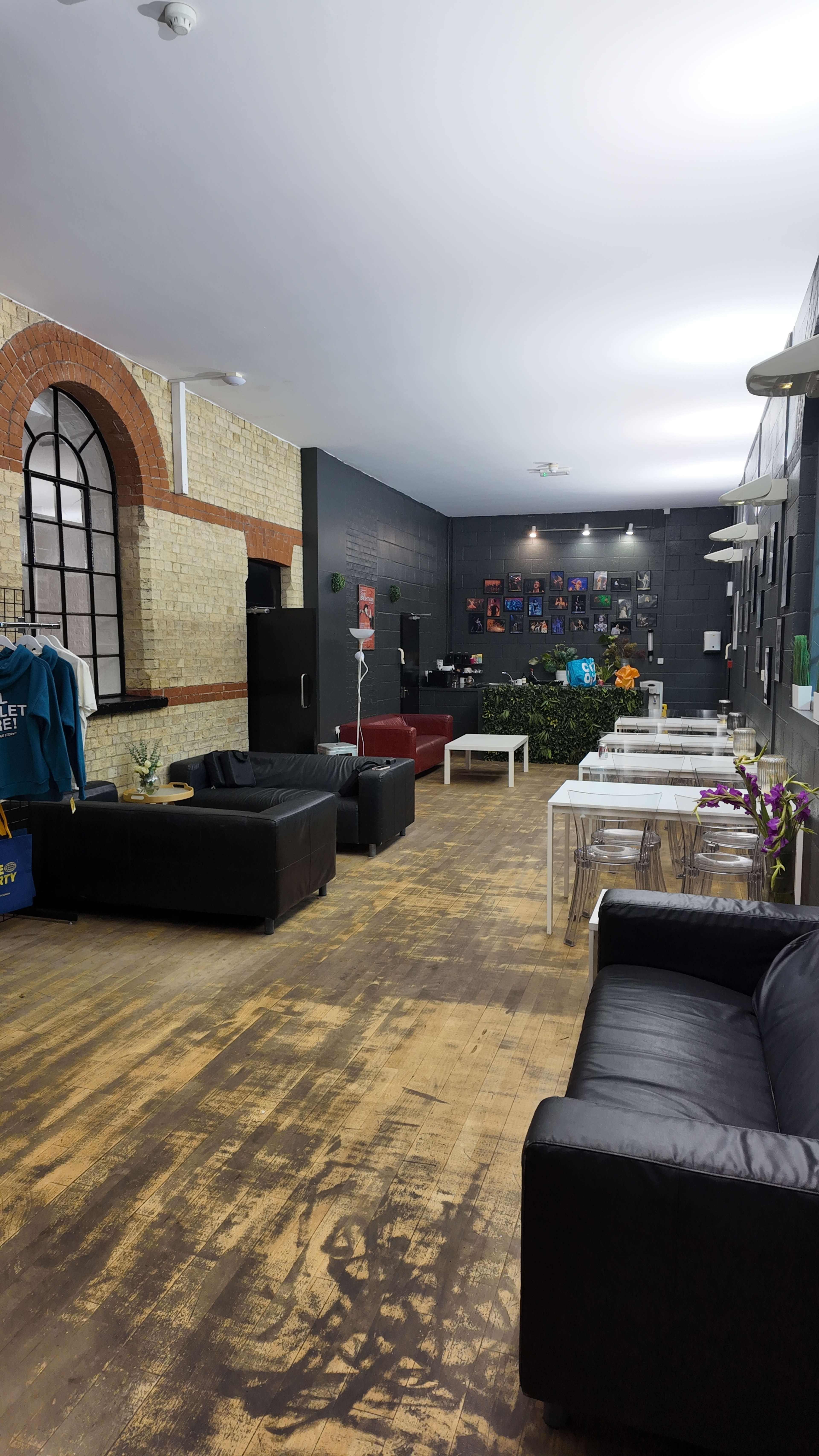 The image shows a spacious, modern lounge area with black leather sofas, a mix of tables, and a wall adorned with colorful photographs.