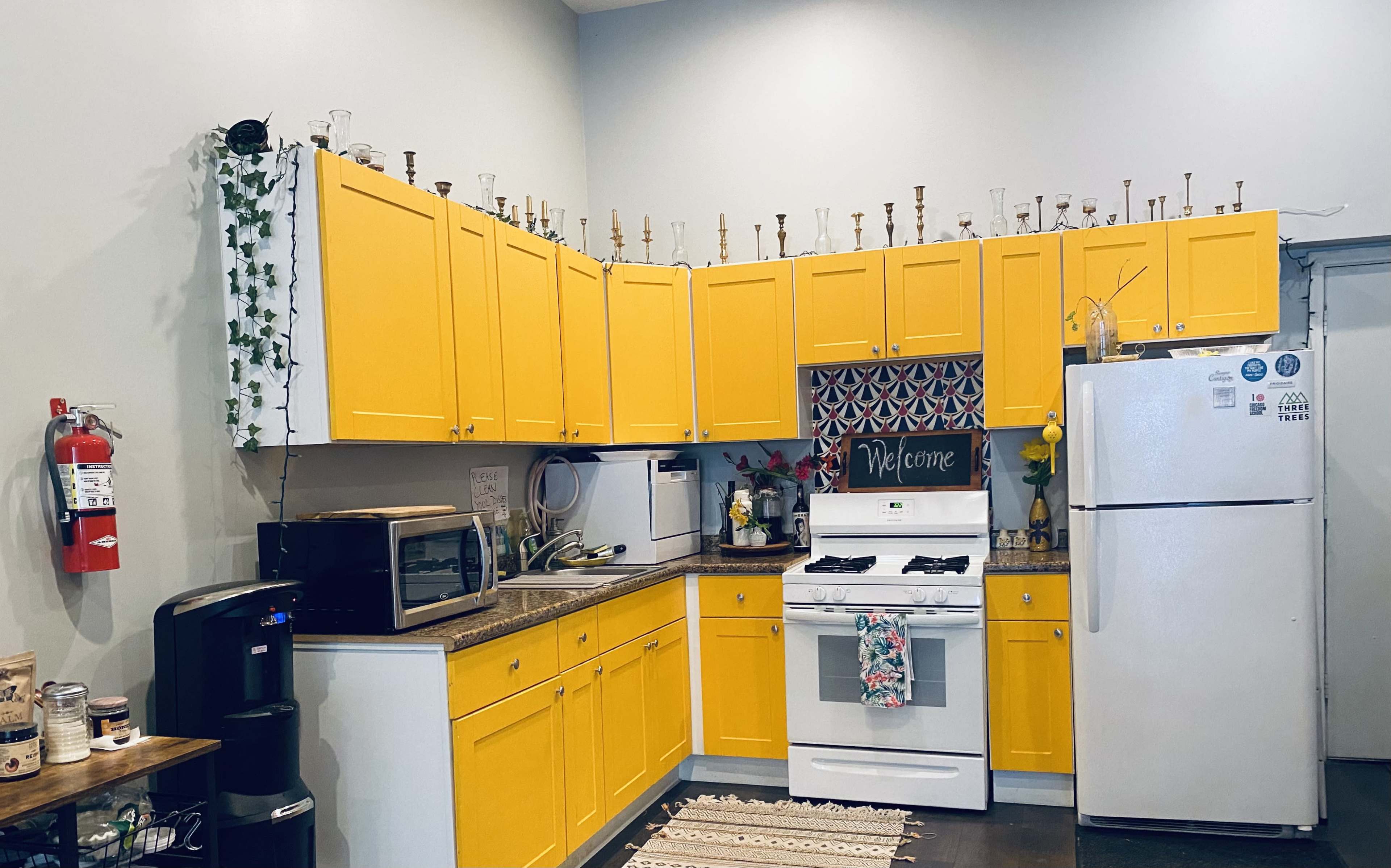 A kitchen with yellow cabinetry, a white stove, a white refrigerator, and various items arranged on the countertop and shelves.