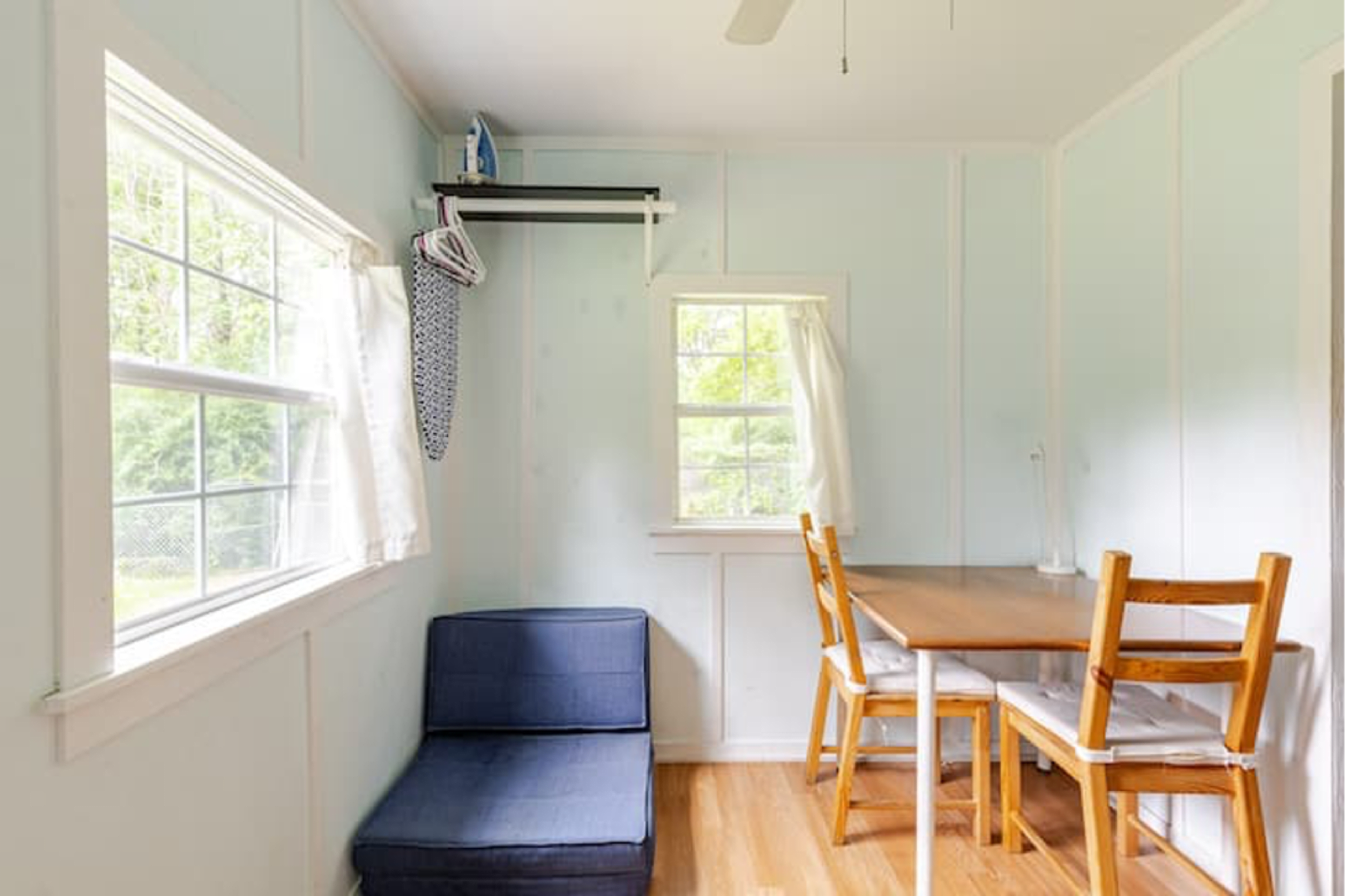 A light blue room with a small table and chairs, a couch in one corner, and windows letting in natural light.