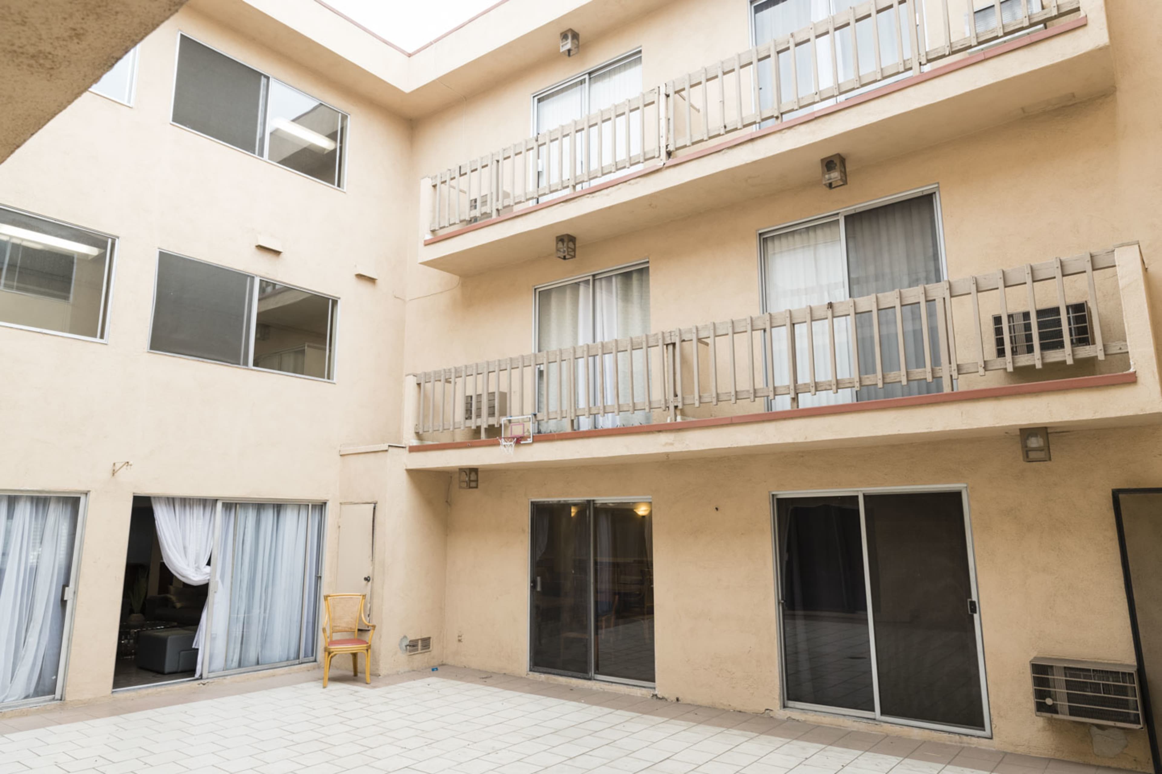 The image shows a small outdoor courtyard surrounded by three stories of beige apartment units, each featuring balconies and sliding glass doors.
