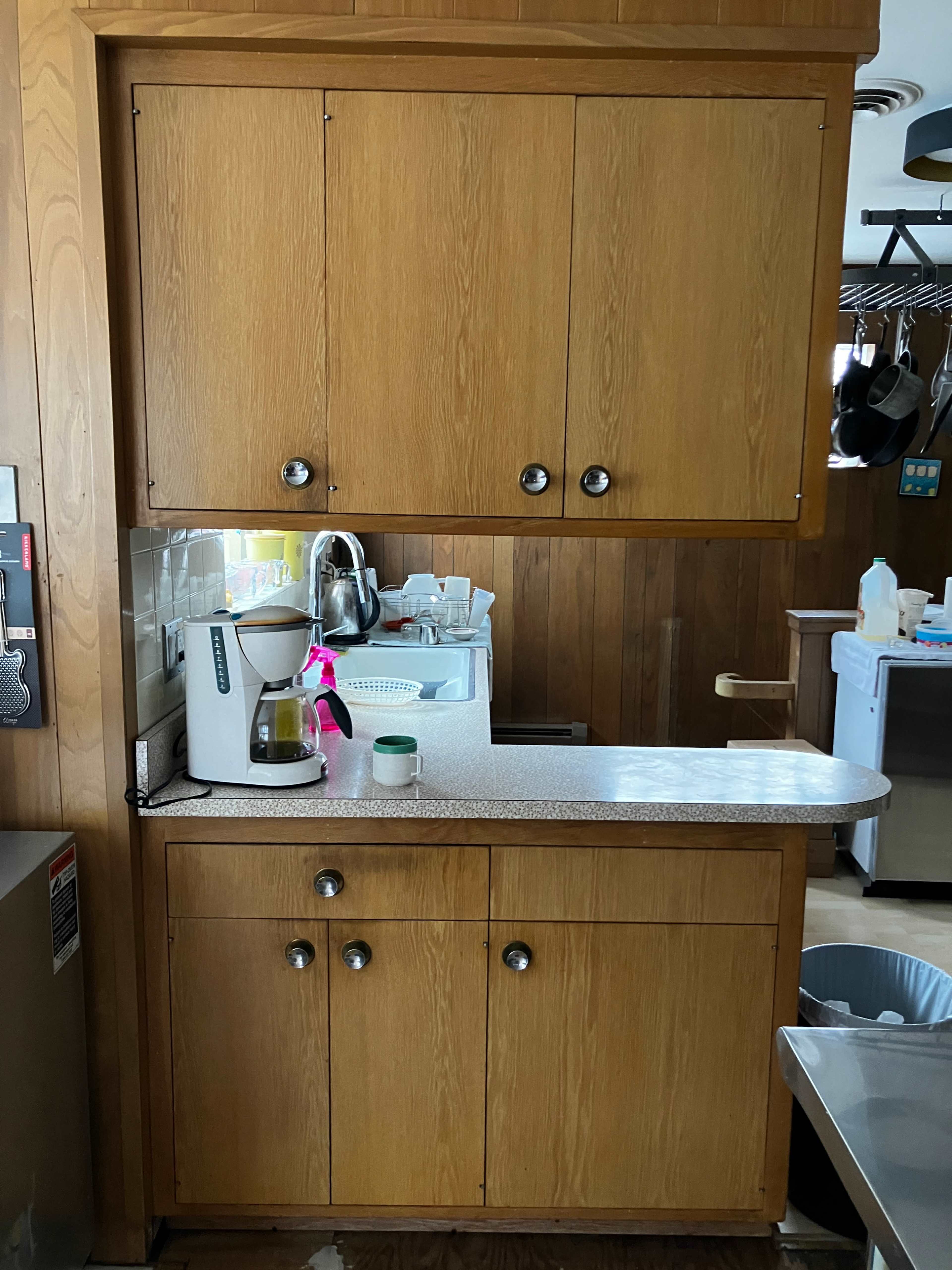 The image shows a wooden kitchen cabinet with upper and lower doors, a countertop, and a coffee maker positioned on the surface.