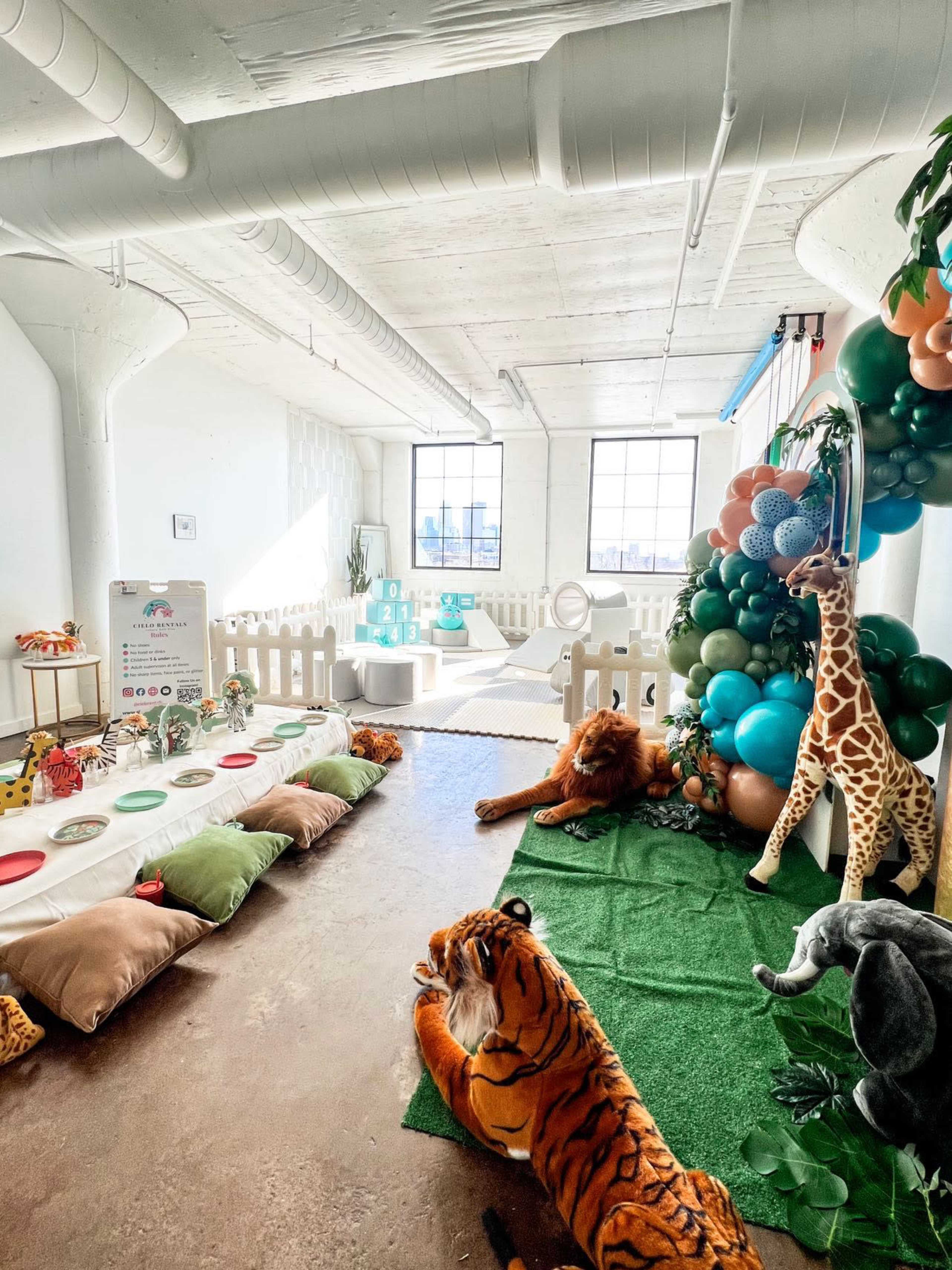 The room features a play area decorated with stuffed animals, balloons, and a soft green carpet.