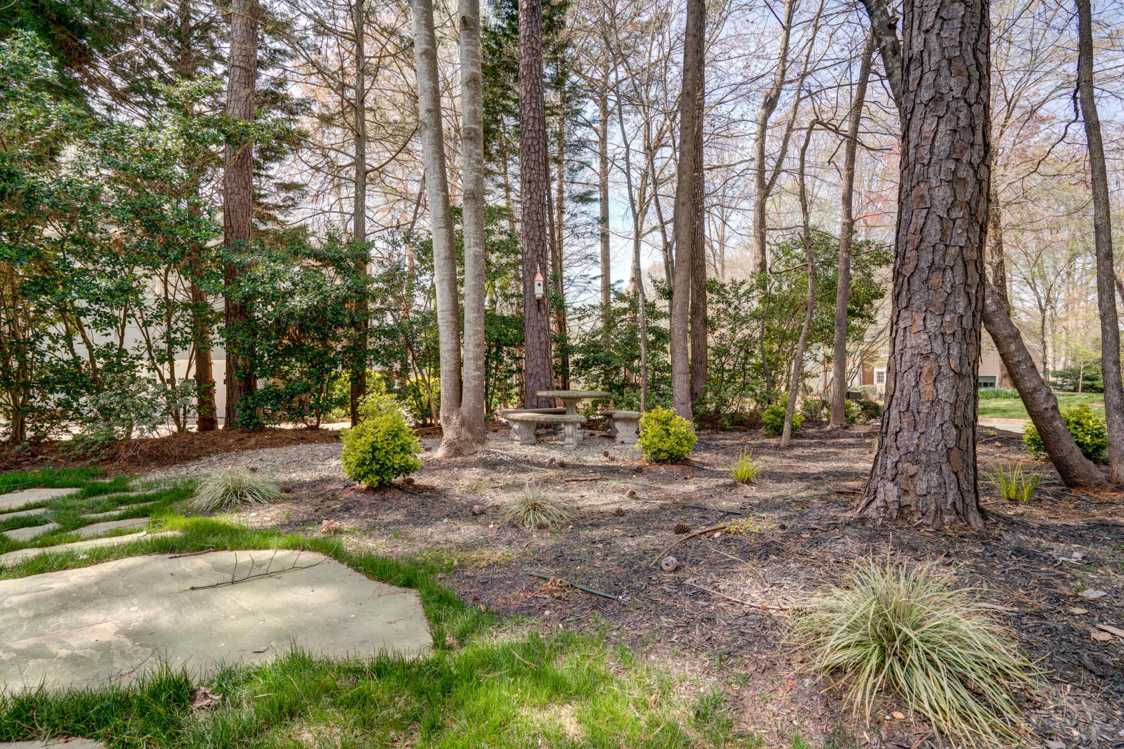 A stone table and bench are surrounded by grass and trees in a landscaped garden area.