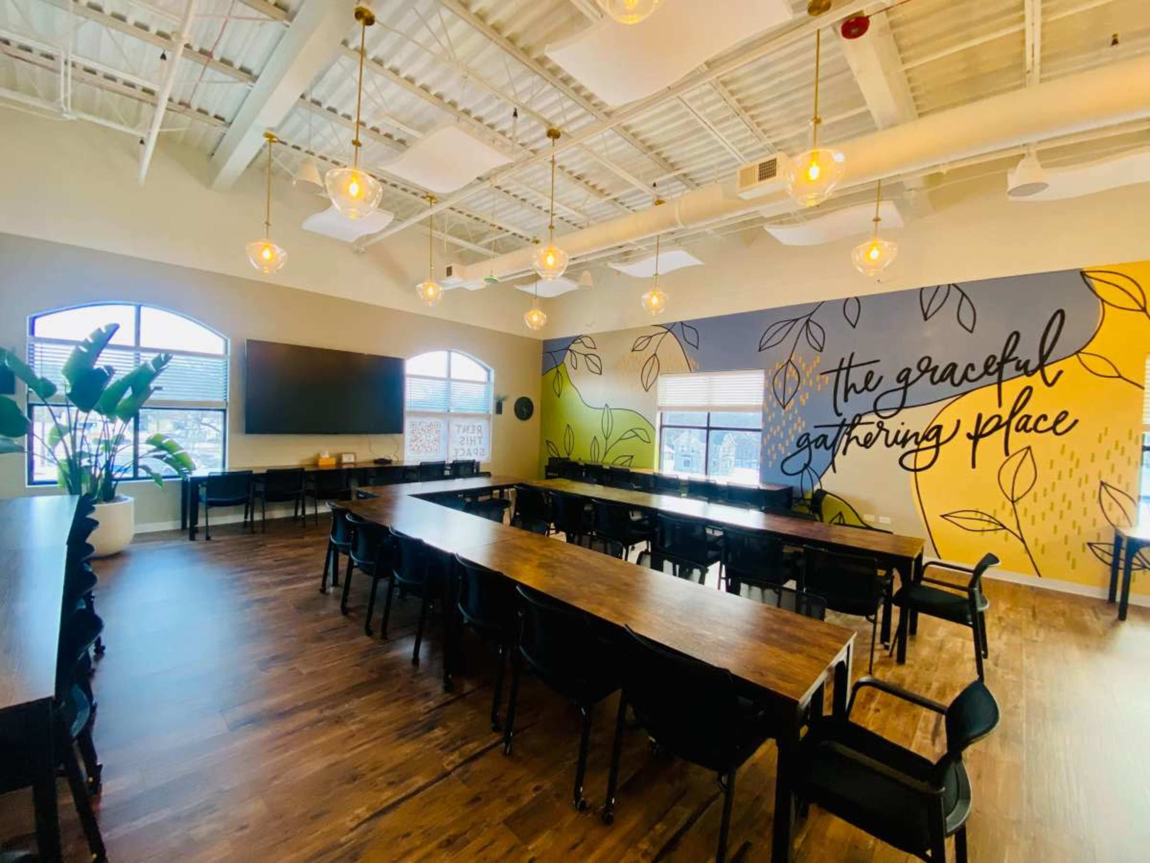 The image shows a spacious, well-lit meeting room with a large wooden table surrounded by black chairs, and a colorful mural on one wall.