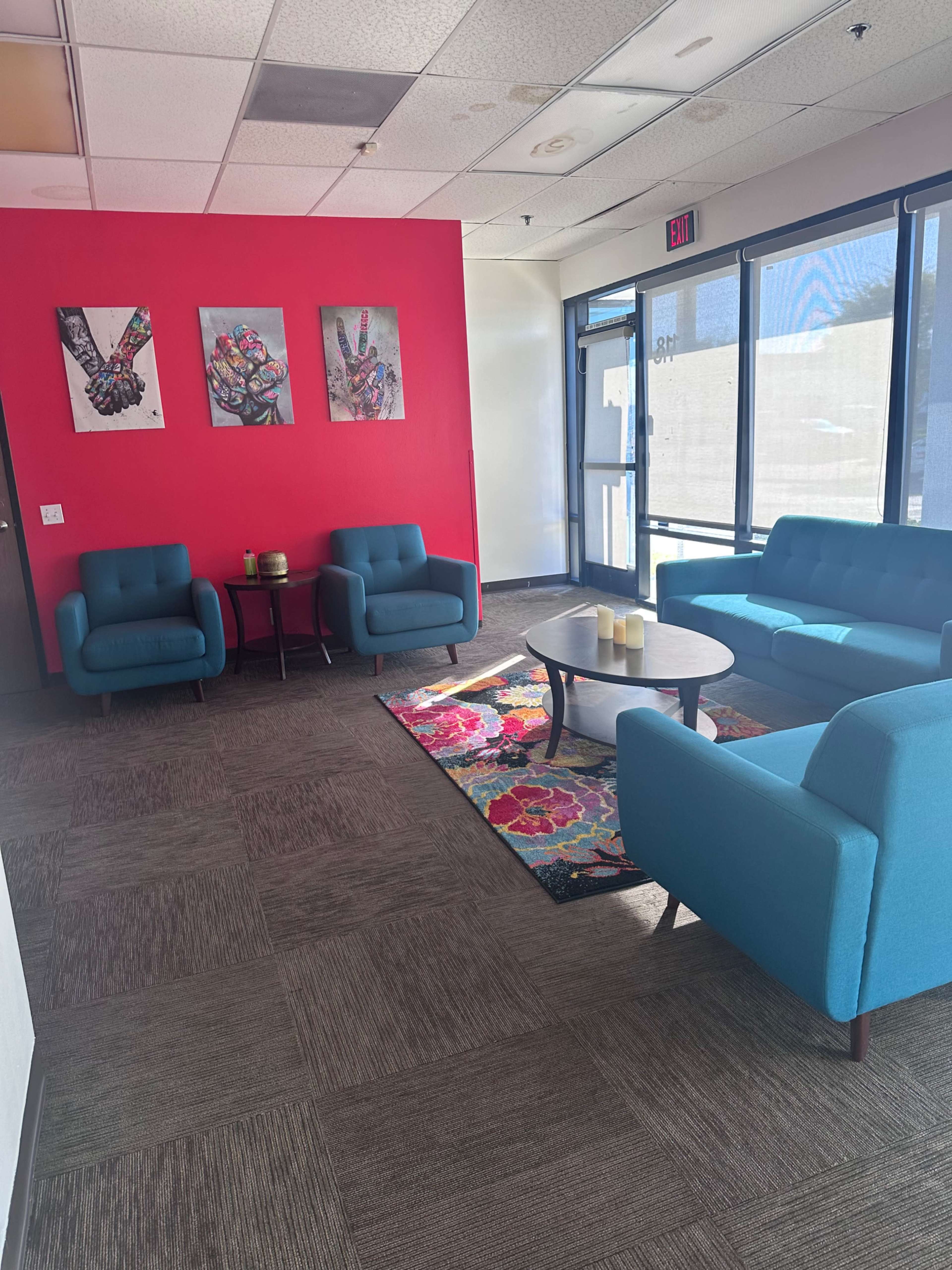 The image shows a modern waiting area with turquoise furniture, a round table, and colorful art on the red wall.