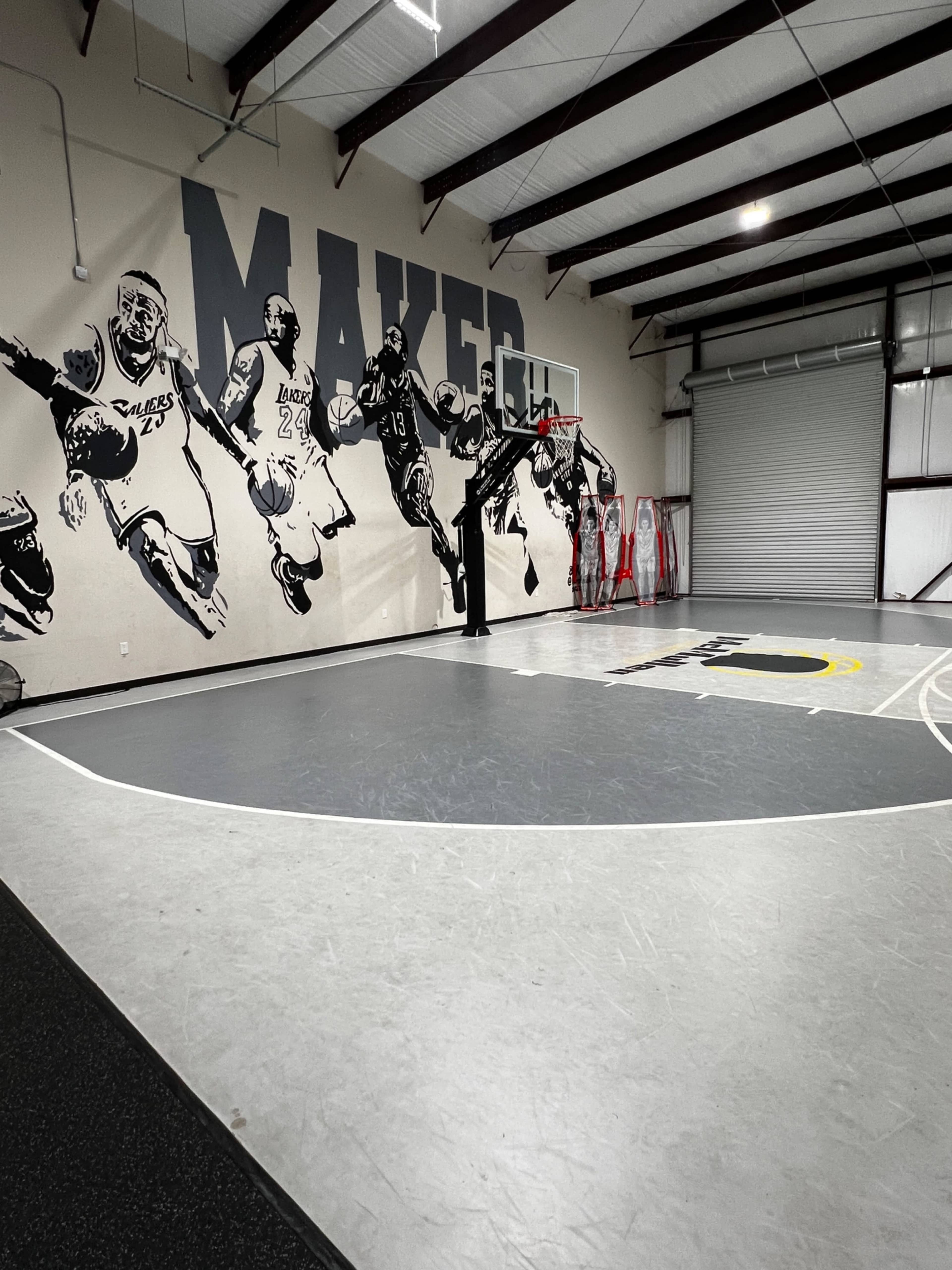 The image shows a basketball gym with a mural of players on the wall and a court marked with lines and logos.
