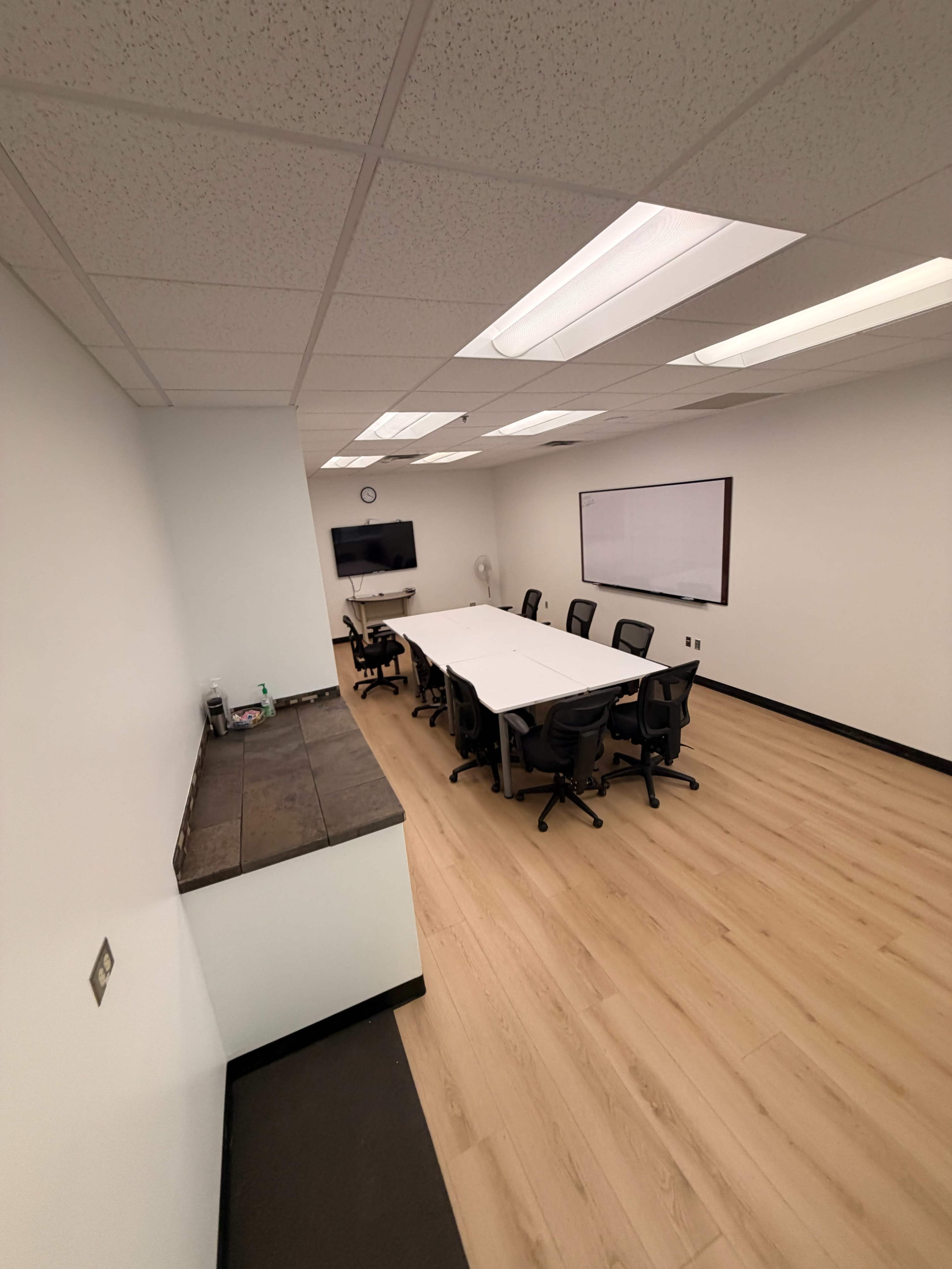 The image shows a spacious conference room with a long table, surrounded by office chairs, and a whiteboard on the wall.
