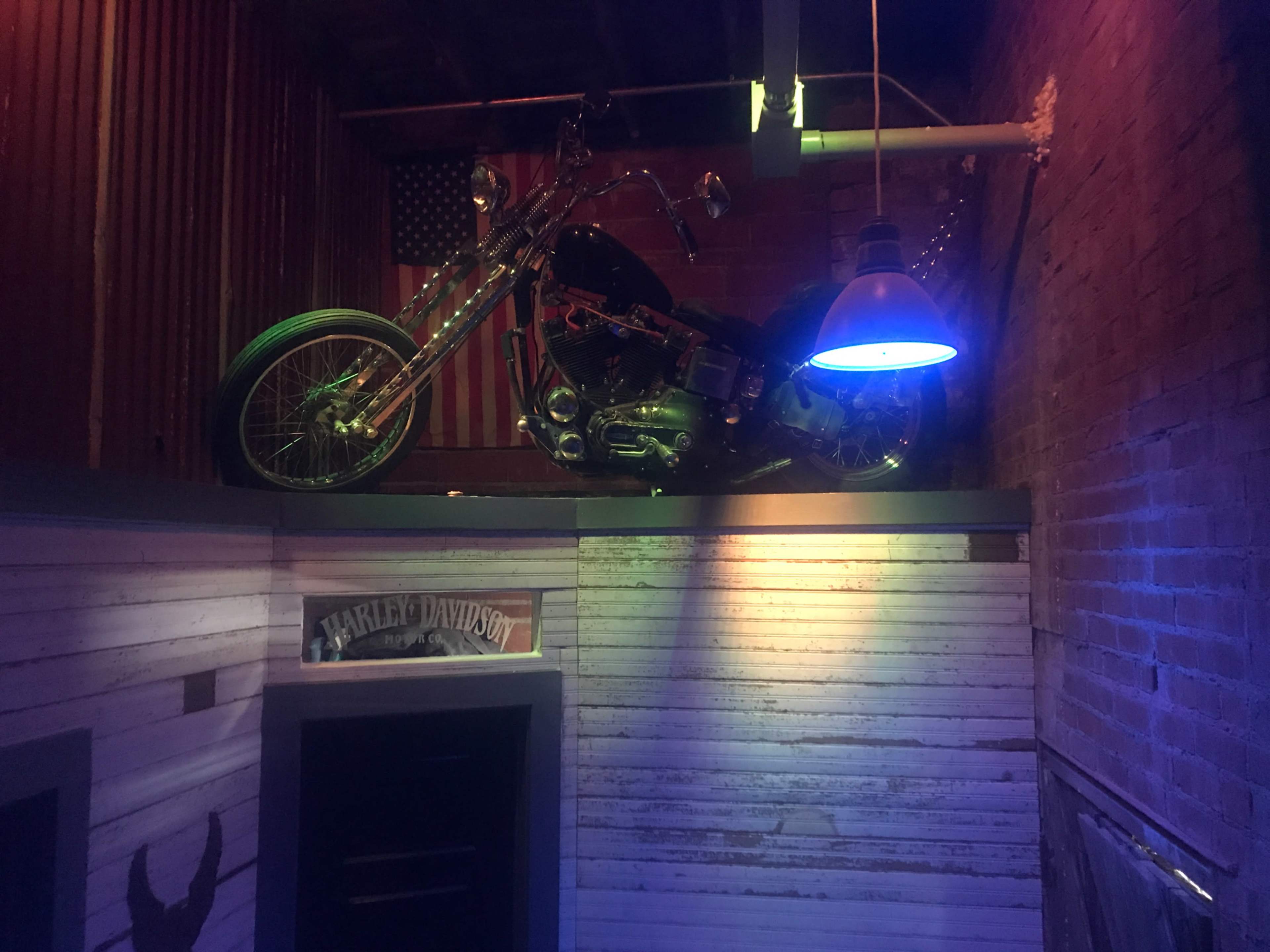 A motorcycle is displayed on a ledge in a rustic room illuminated by a blue pendant light.