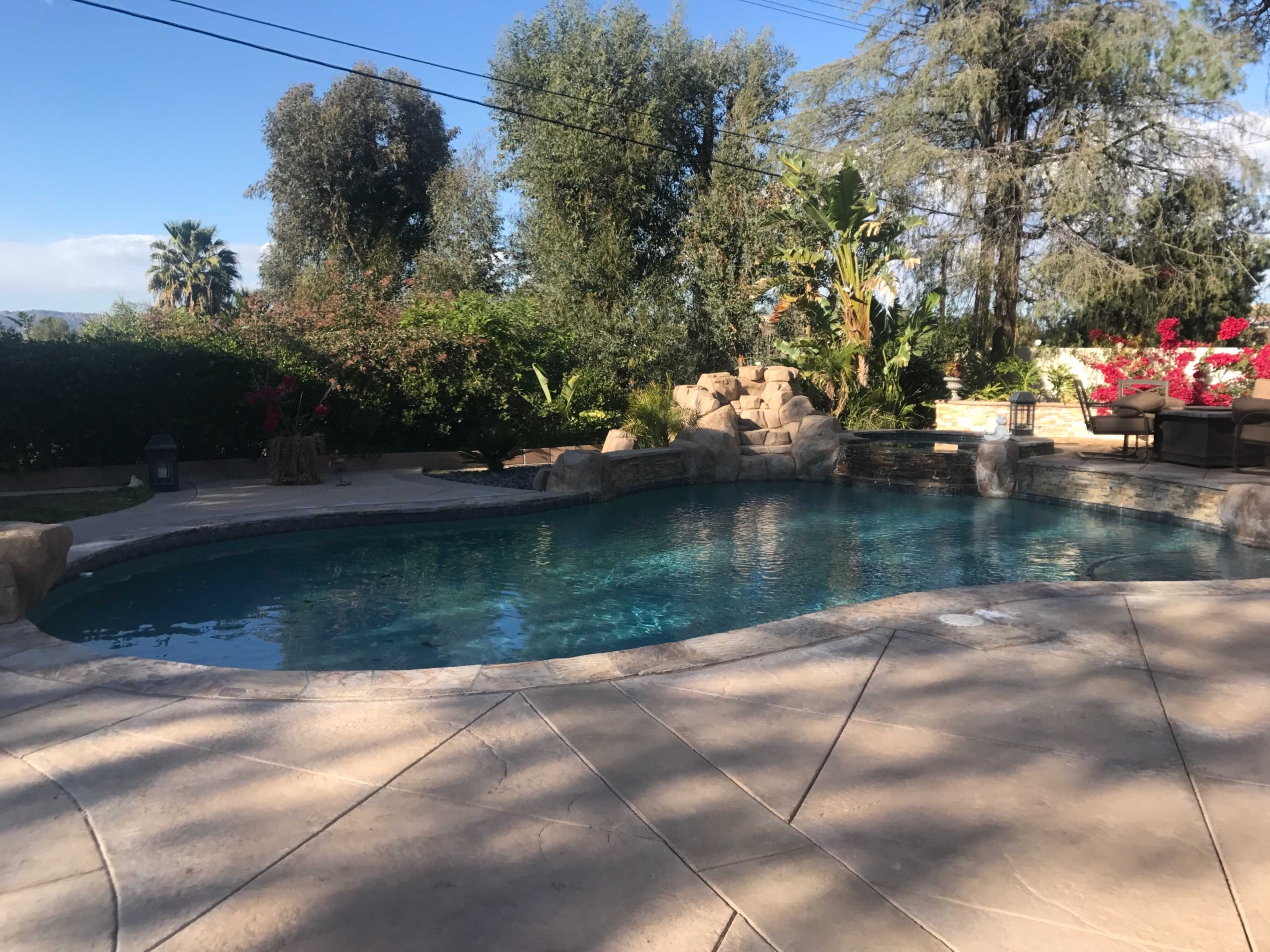 A landscaped backyard features a swimming pool surrounded by stone accents and lush greenery.