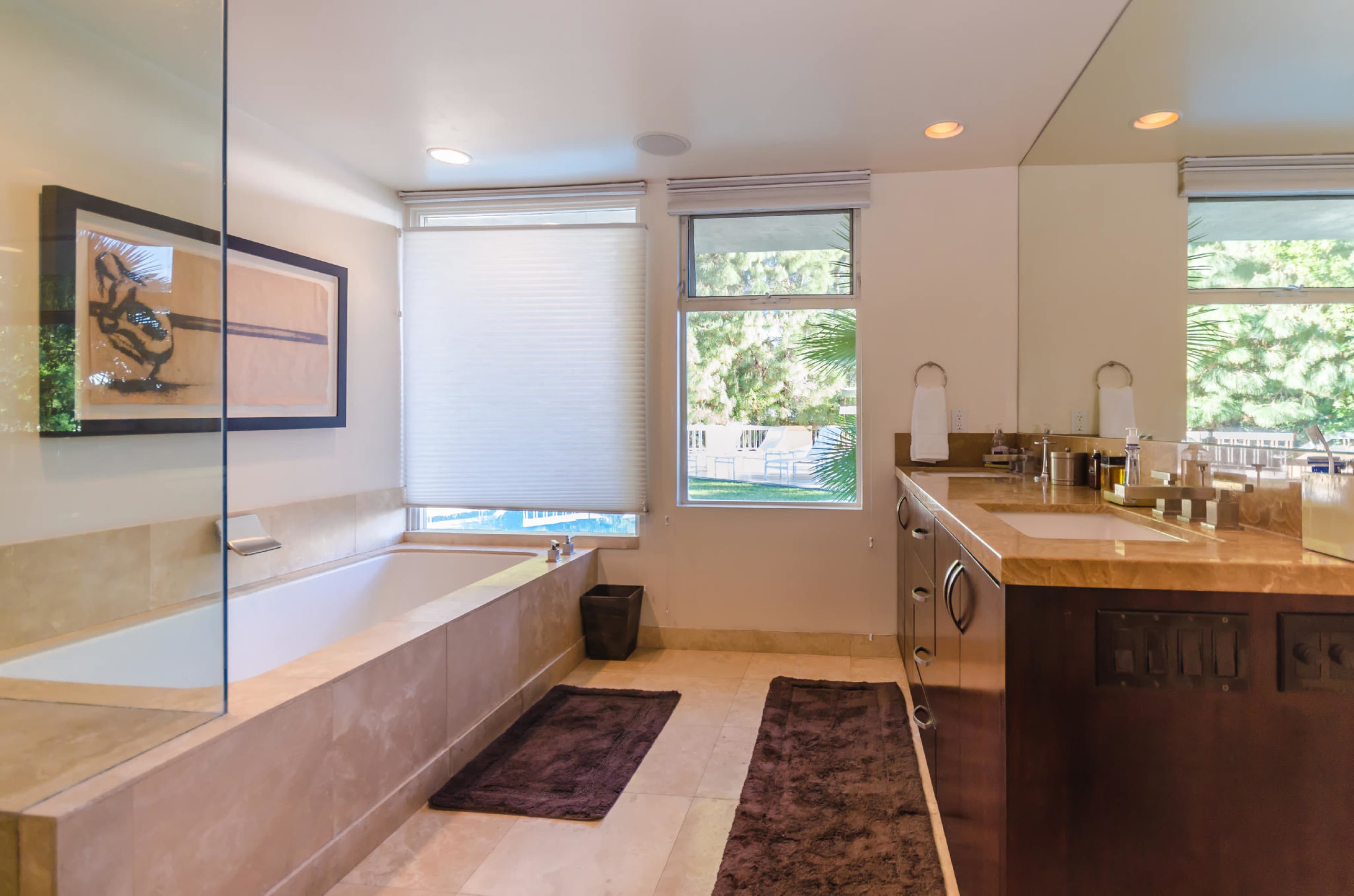 The image showcases a modern bathroom featuring a freestanding bathtub, a double vanity, and a large window with natural light.