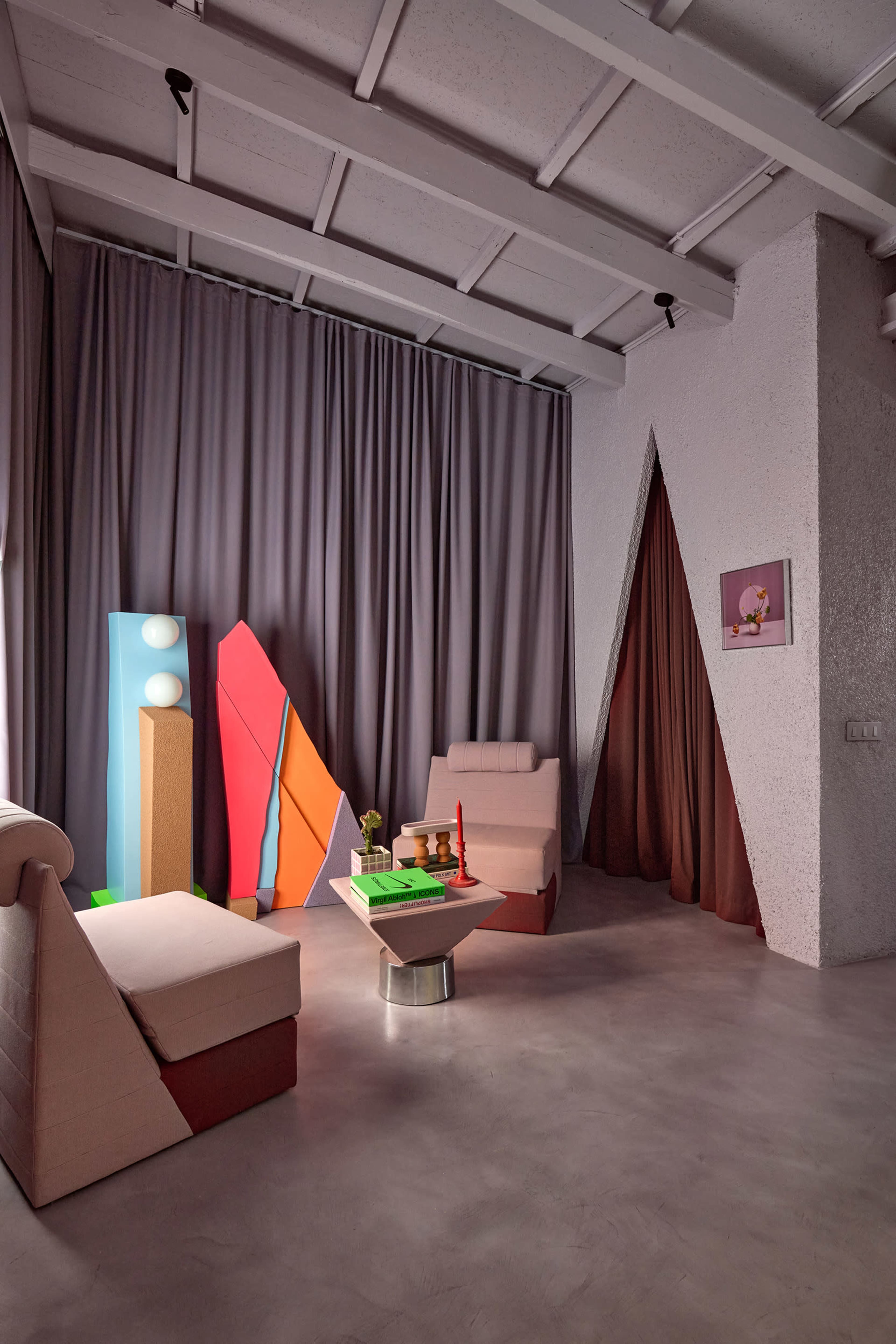 The image shows a modern living room with abstract colorful decor, featuring two sofas, a low coffee table, and a backdrop of gray curtains and textured walls.