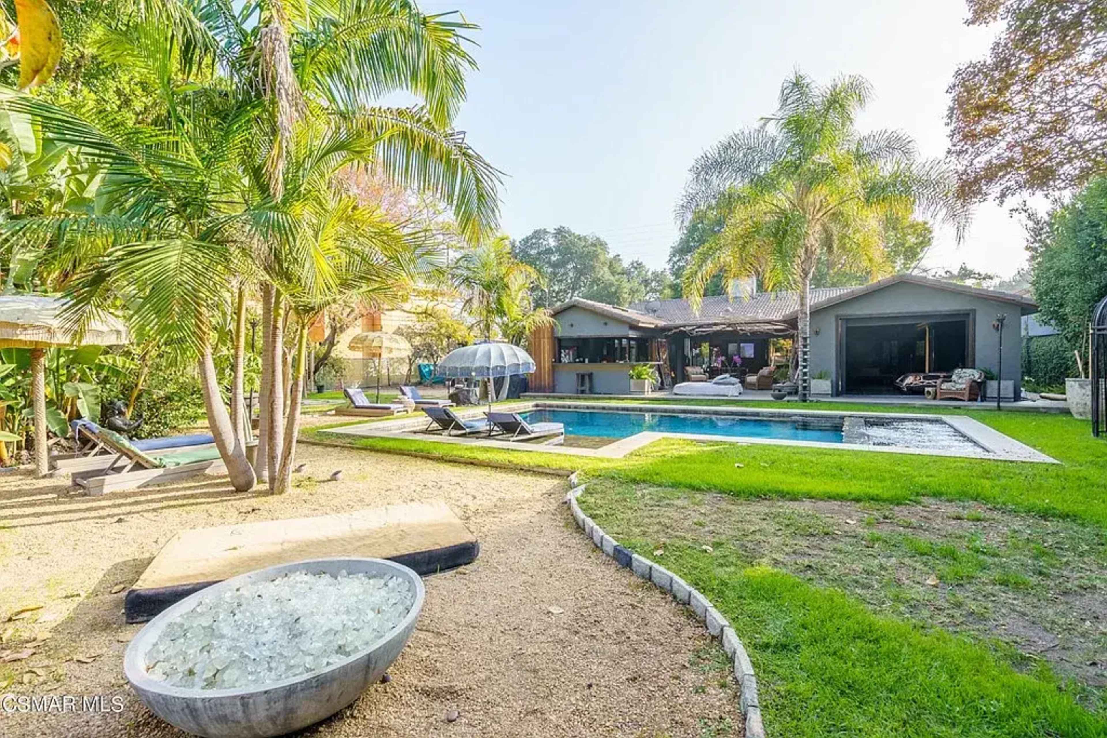 The image shows a backyard with a swimming pool, lounge chairs, palm trees, and a house in the background.