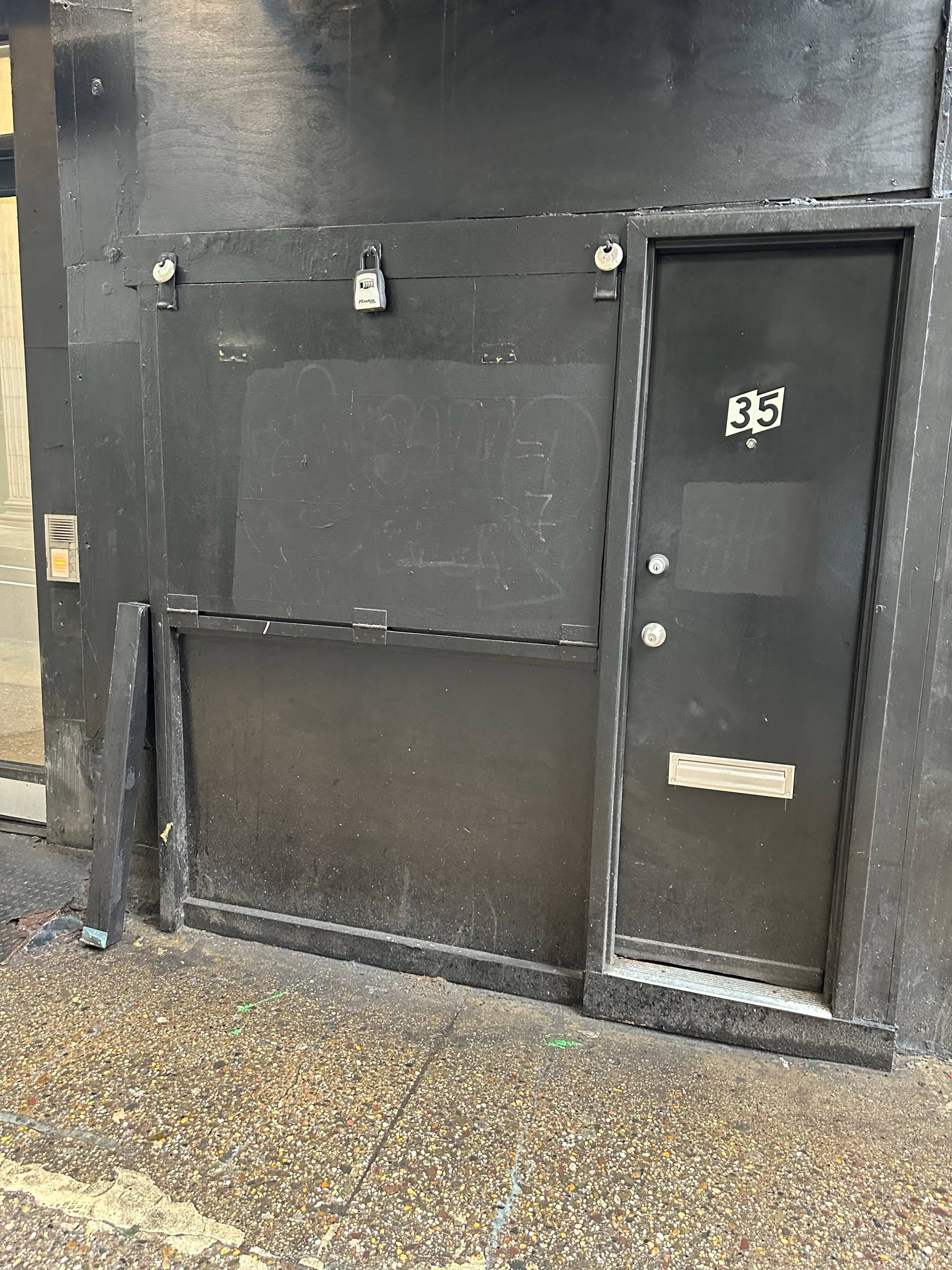 The image shows a black wall with a door marked "35" and an area that appears to be covered in graffiti or markings.